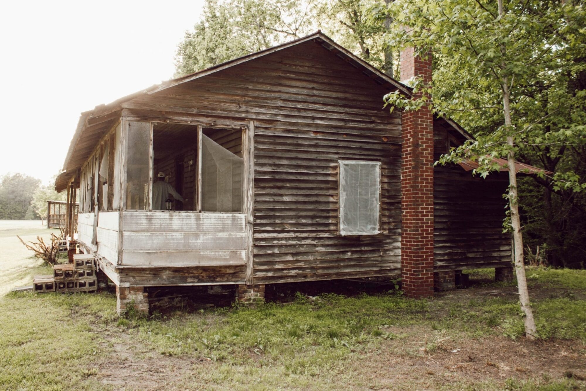 1800's NC farmhouse with weathered wood siding, red brick chimney, and screened in porch