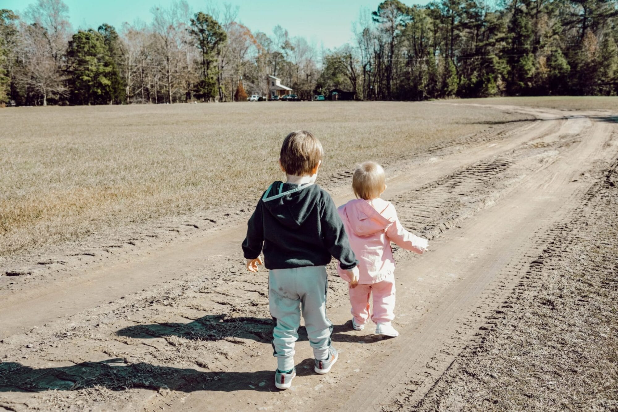 two toddlers walking on a dirt road