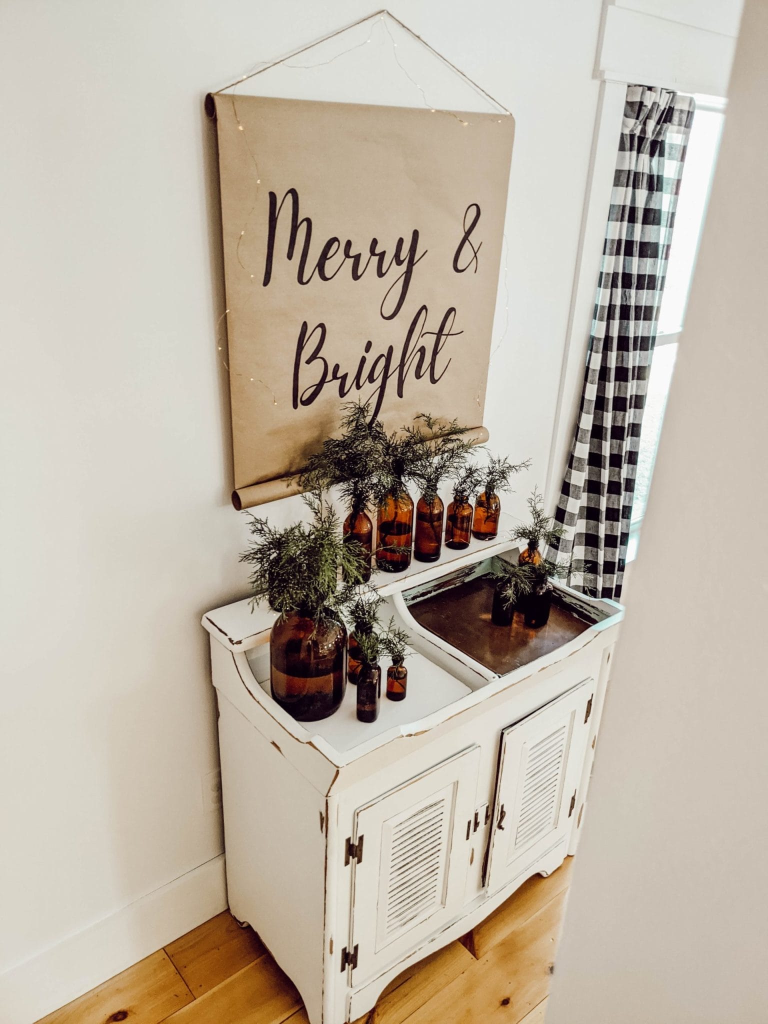 neutral Christmas vignette with farmhouse scroll sign, dry sink, and brown glass bottle collection