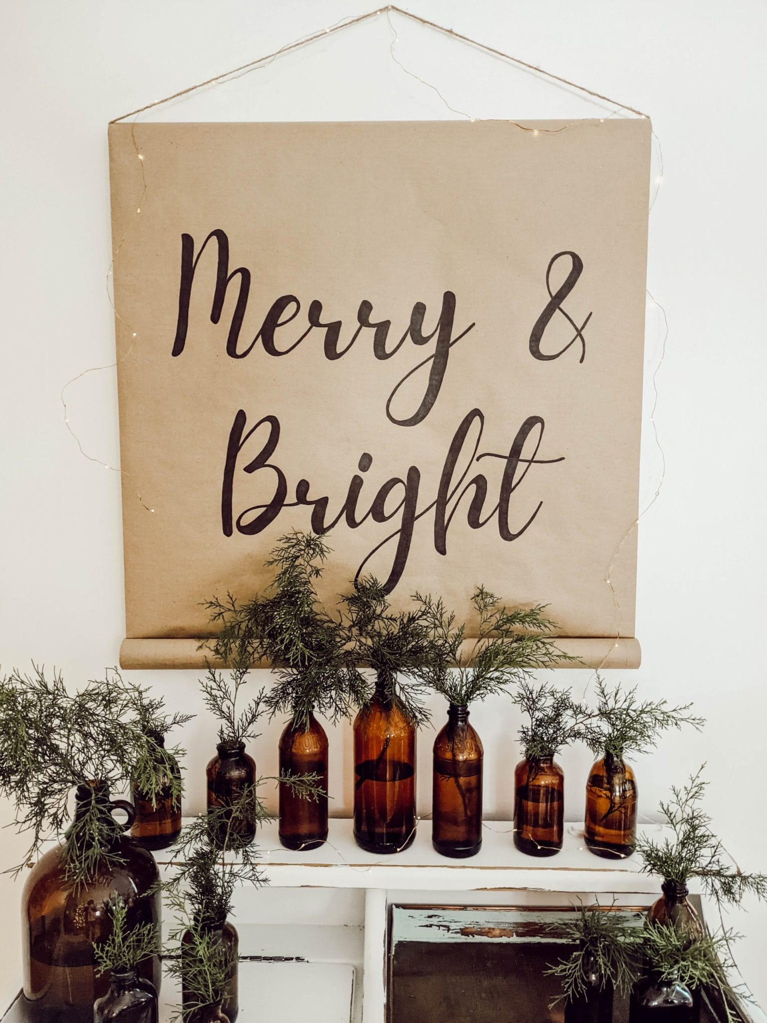 neutral Christmas vignette with farmhouse scroll sign, dry sink, and brown glass bottle collection