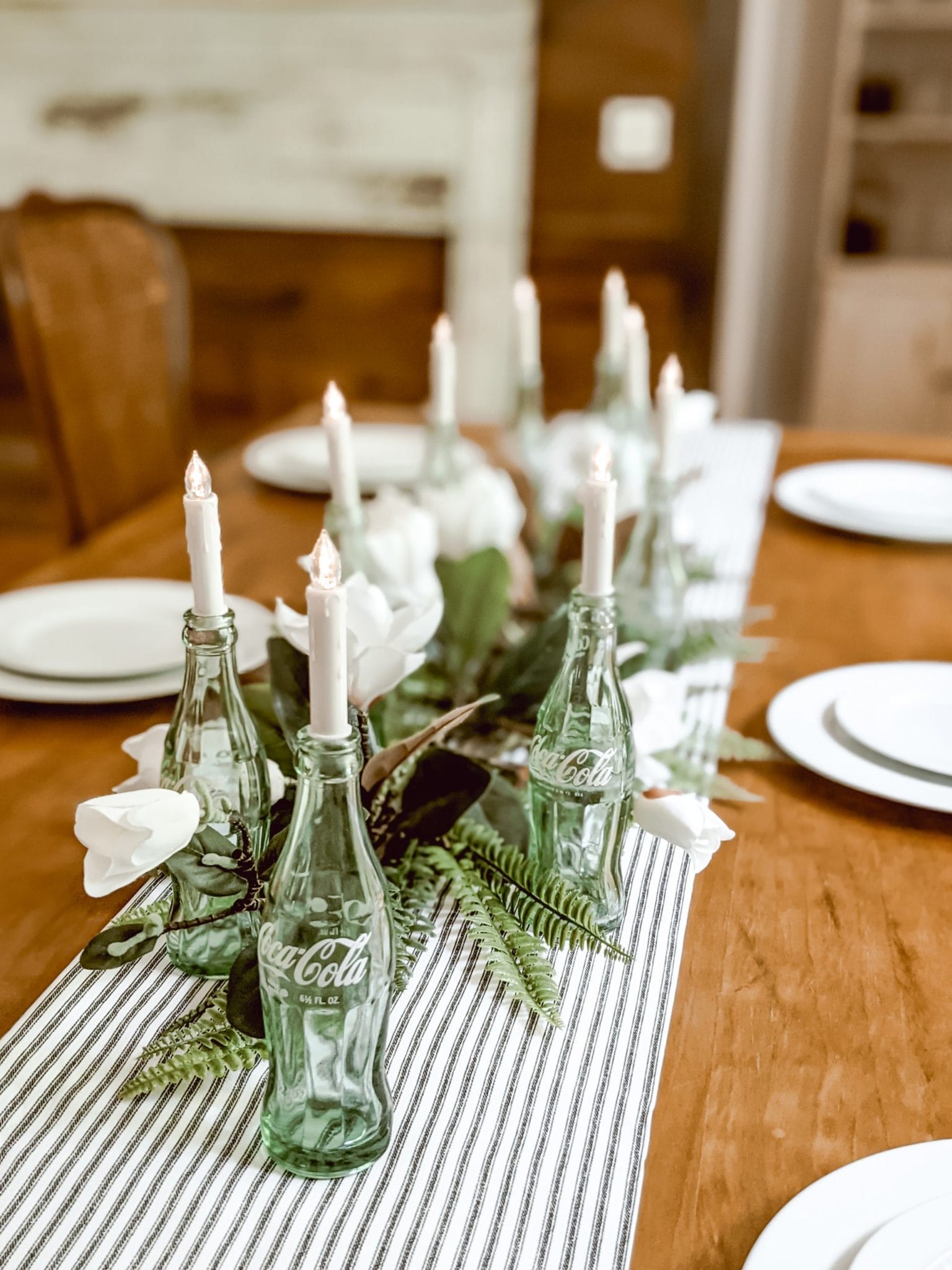 spring centerpiece using ticking stripe table runner, coca cola bottles, candles and faux magnolias and ferns