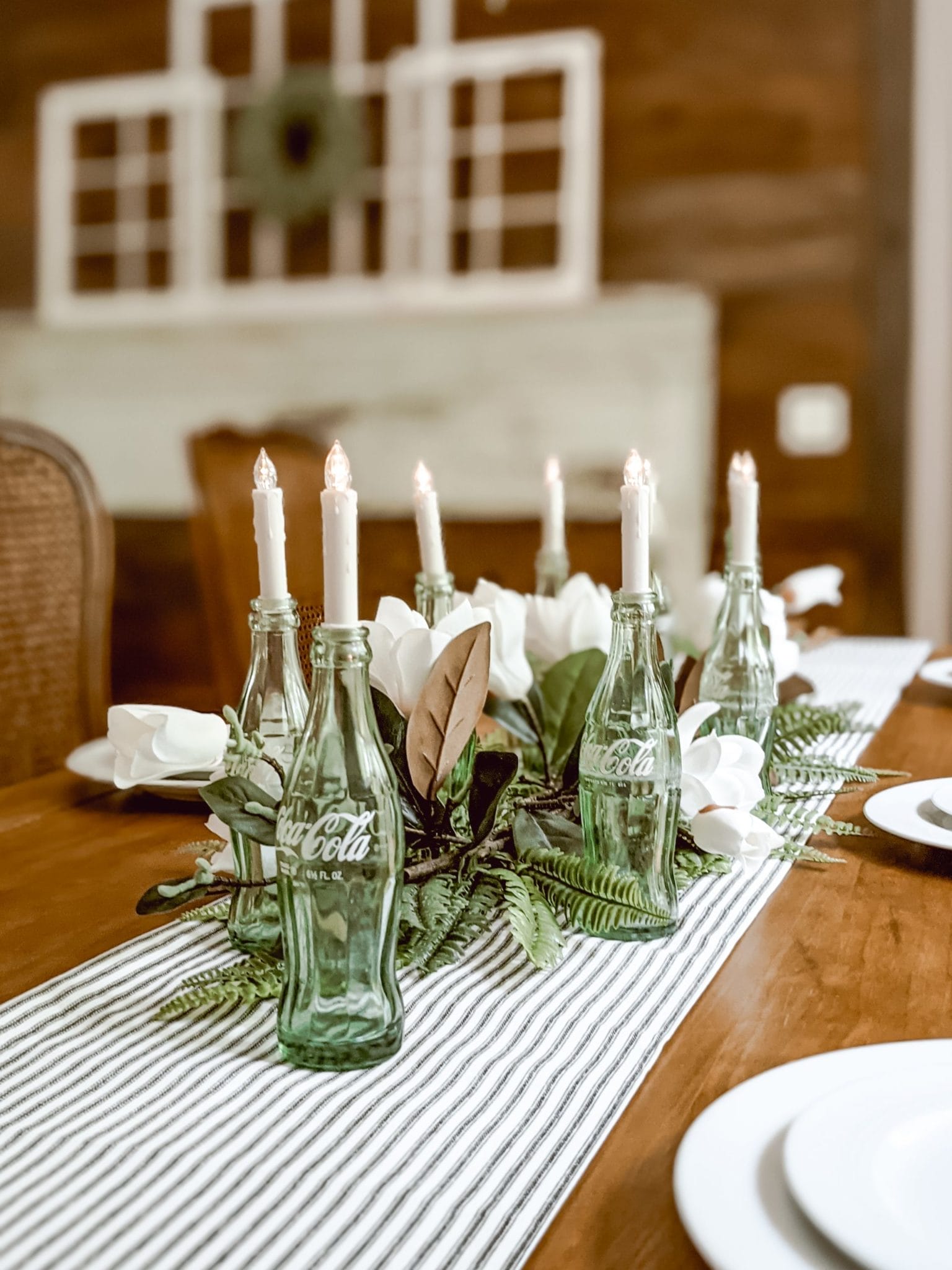 spring centerpiece using ticking stripe table runner, coca cola bottles, candles and faux magnolias and ferns