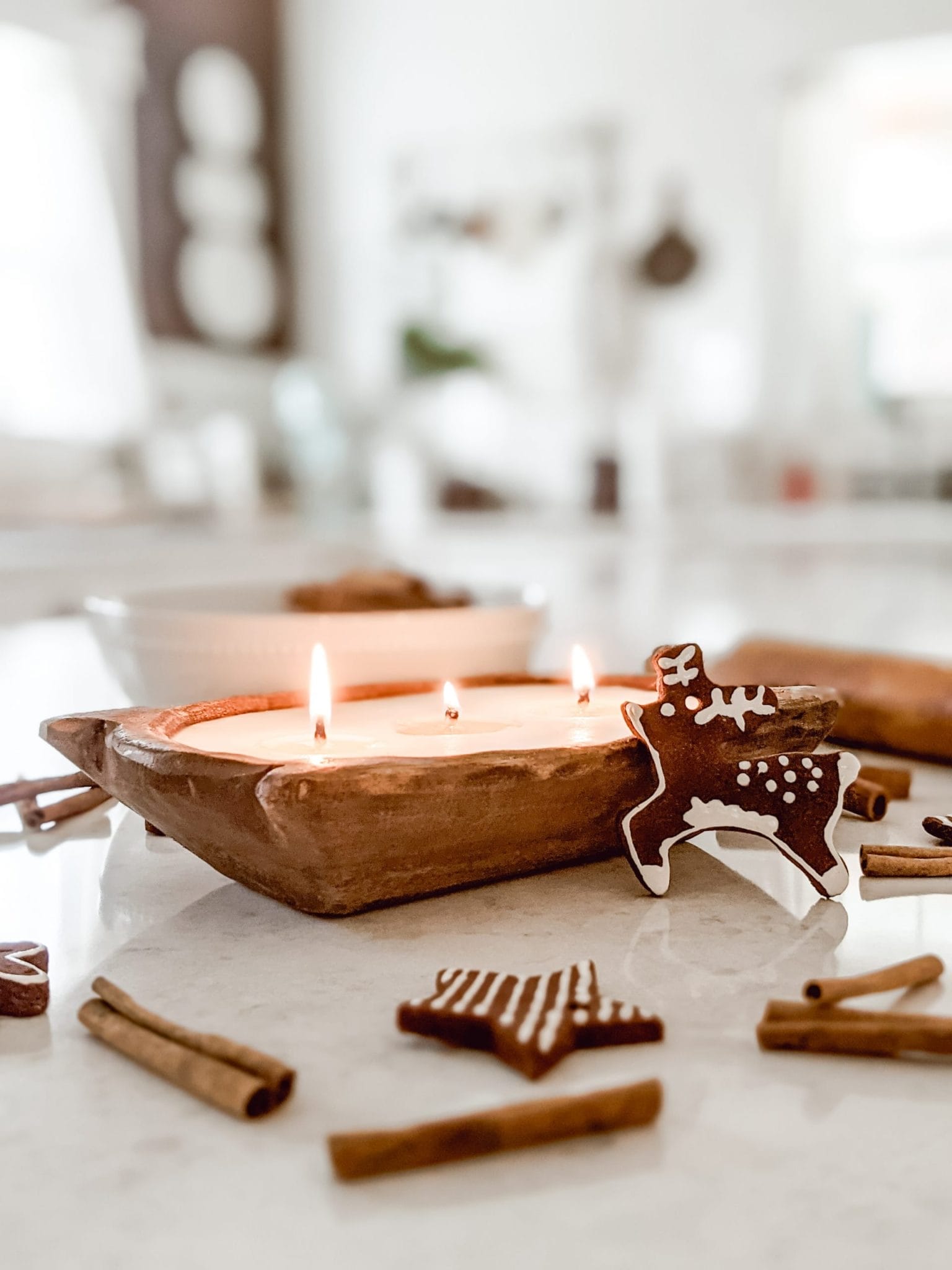 gingerbread cookie Christmas ornament shaped like a reindeer in front of a wooden dough bowl candle
