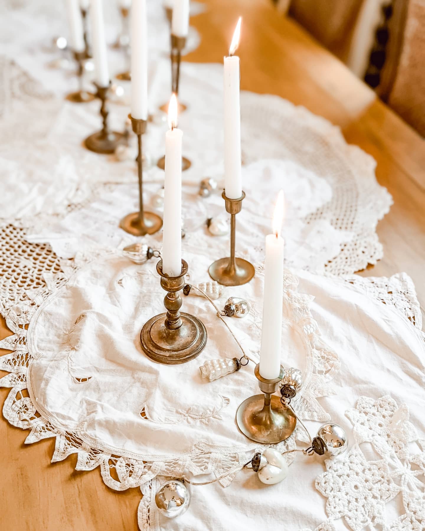 white Christmas tablescape with vintage doilies, brass candlesticks, and a mercury glass ornament garland