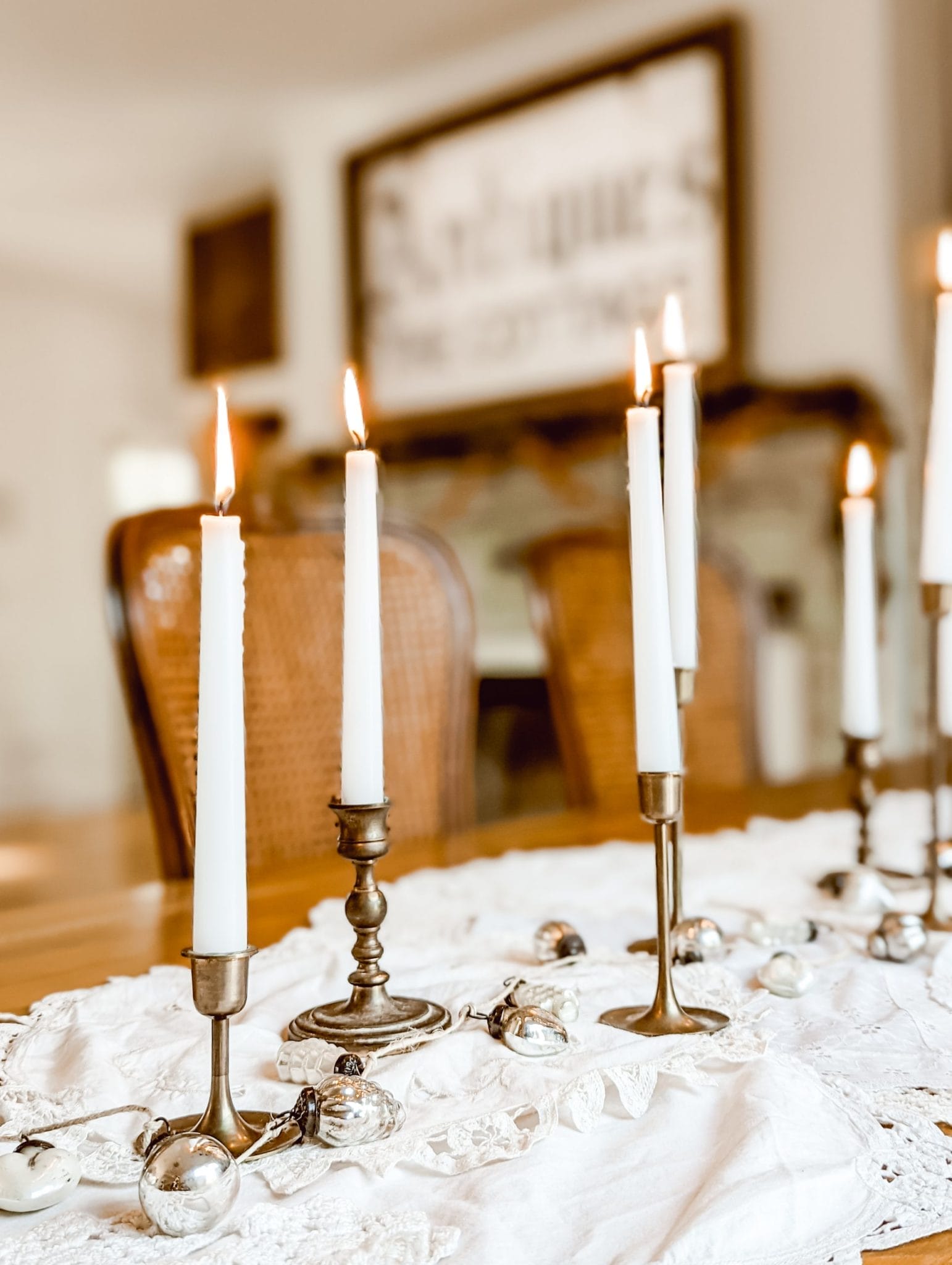 white Christmas tablescape with vintage doilies, brass candlesticks, and a mercury glass ornament garland