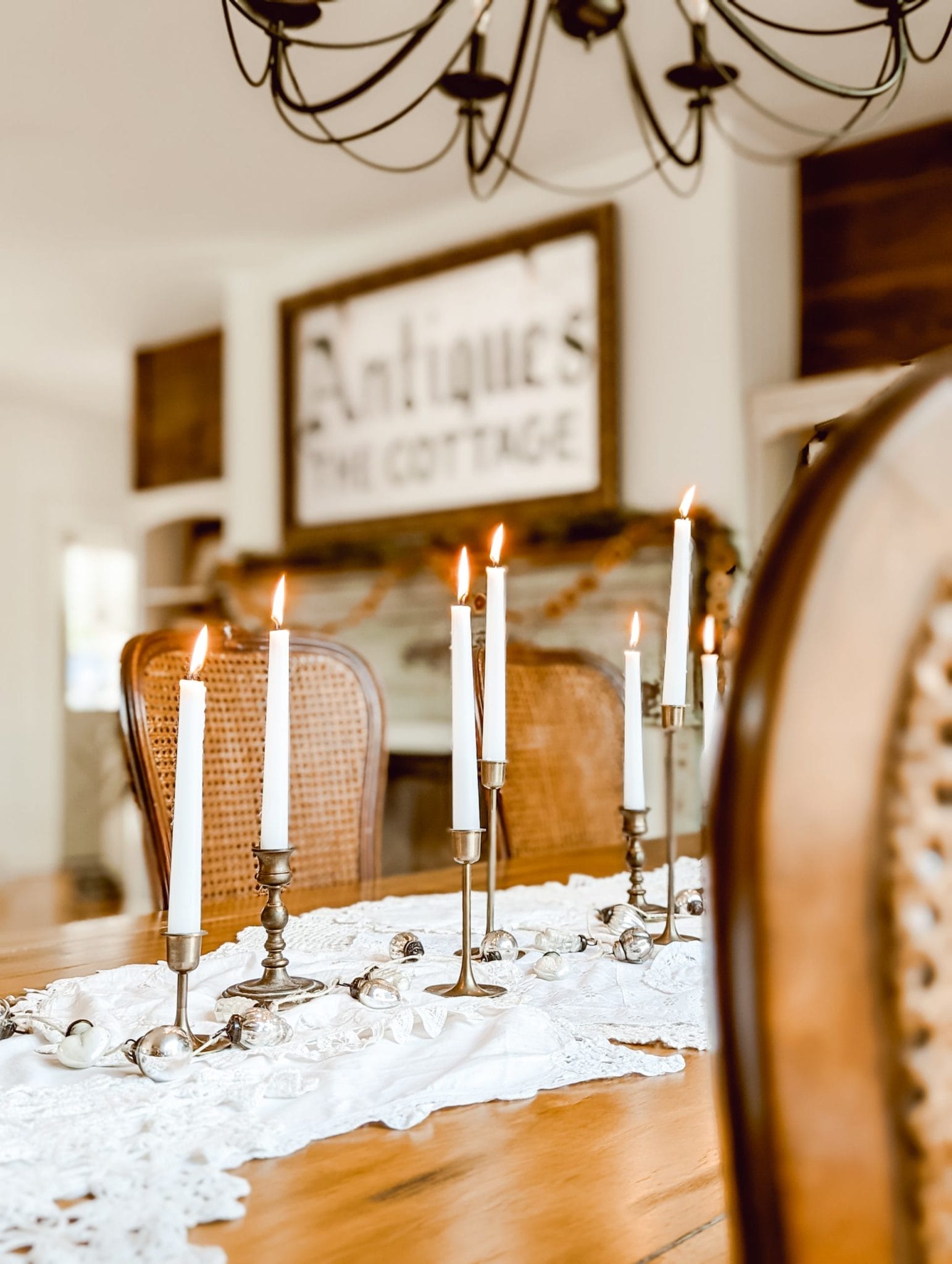 white farmhouse Christmas tablescape with vintage doilies, brass candlesticks, and a mercury glass ornament garland