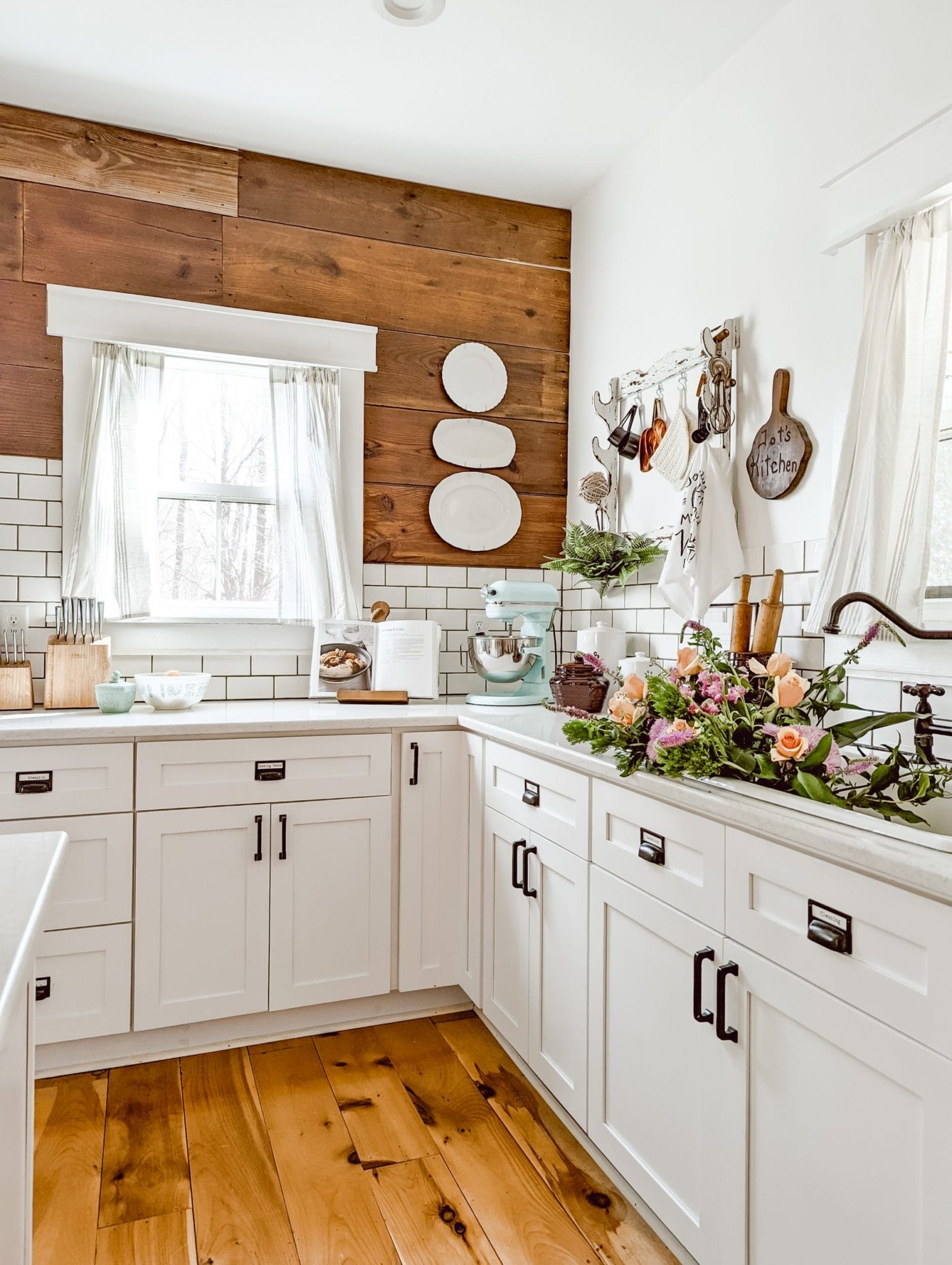 farmhouse kitchen with reclaimed wood shiplap, white shaker cabinets, white subway tile backsplash and spring florals in the sink