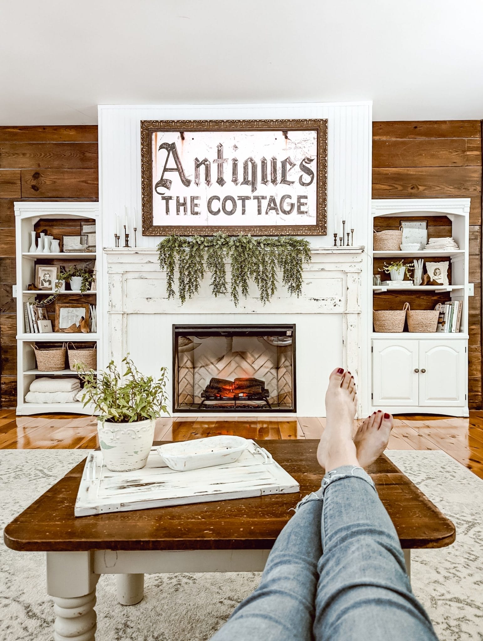 vintage farmhouse and cottage style fireplace with lots of white and wood tones, beadboard, built-in shelves, a chippy white antique mantel, an electric insert, and a Frame TV above the mantel