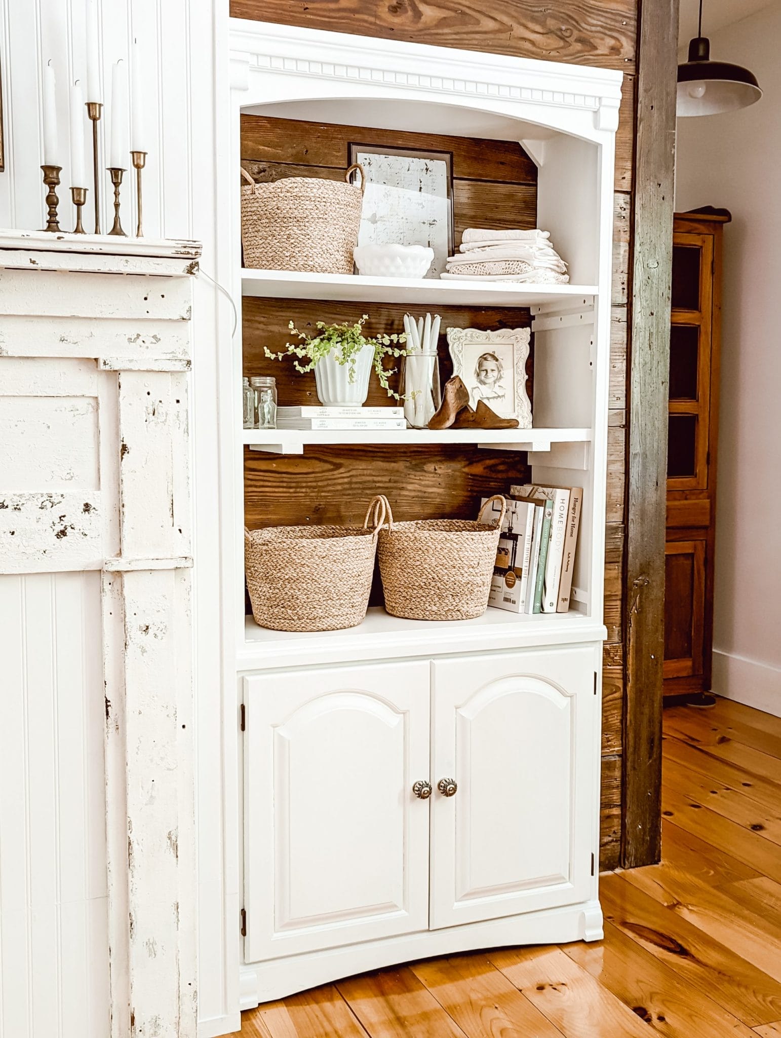 vintage farmhouse and cottage style shelf with framed photos, a stack of doilies, a collection of books, baskets, and a houseplant