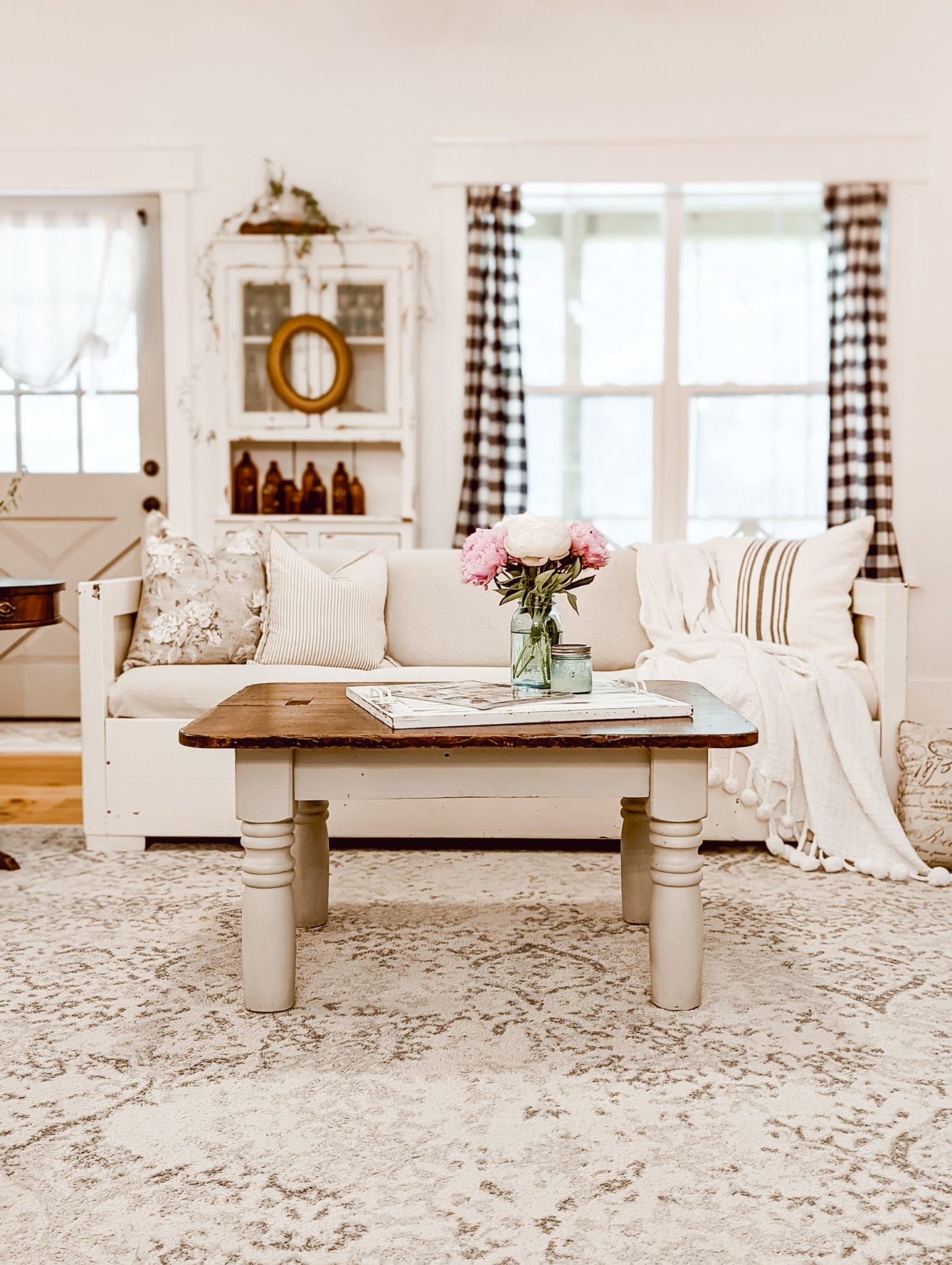 white cottage farmhouse livingroom with painted couch, buffalo plaid curtains, and a two toned coffee table