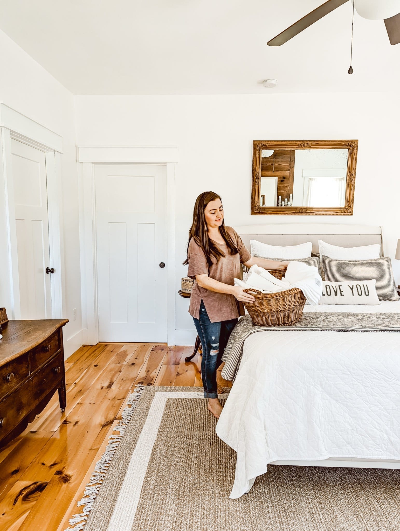 freshly laundered sheets in an antique laundry basket in our white farmhouse cottage style bedroom