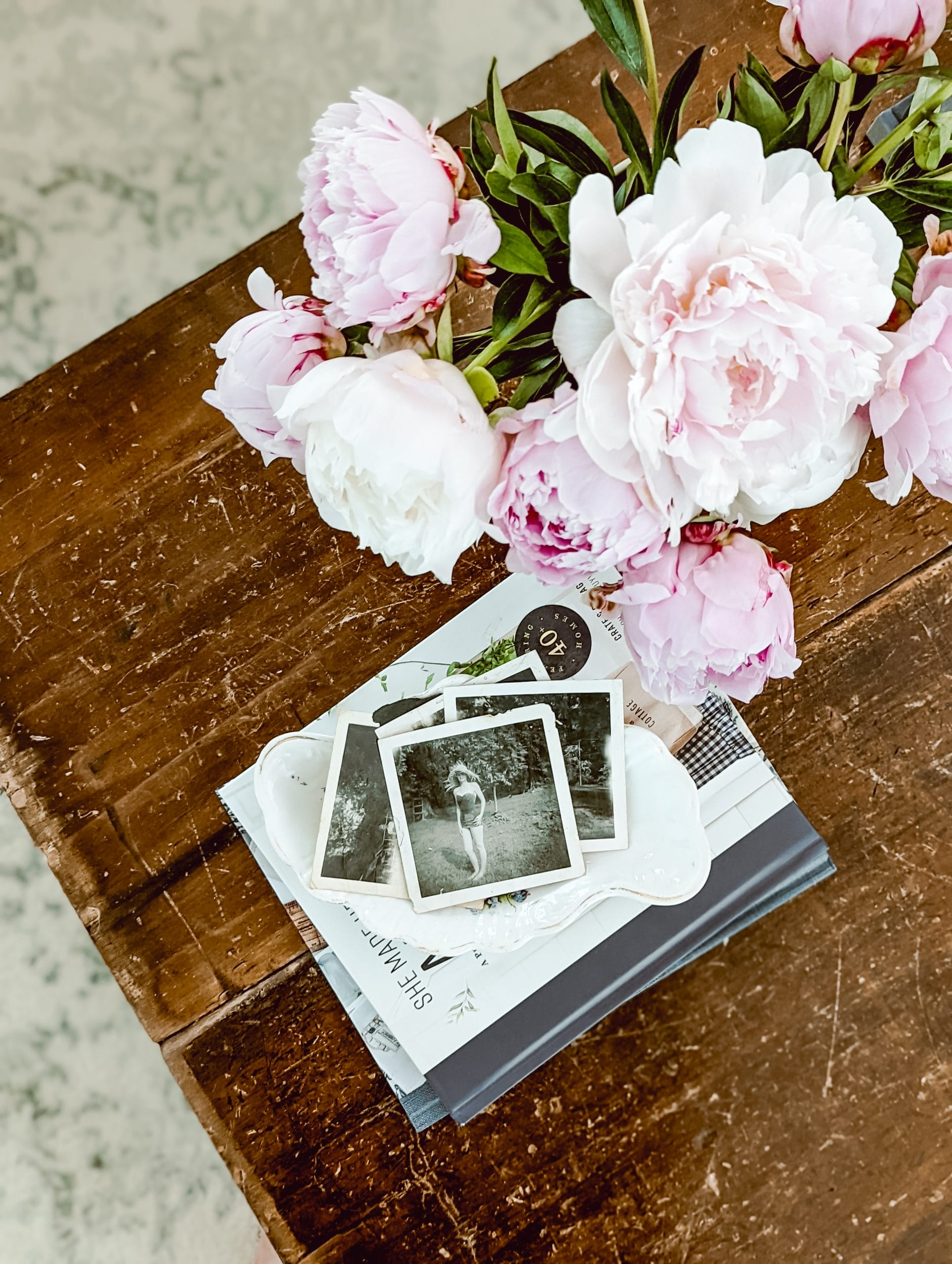 flat lay shot of pink peony arrangement and a few old black and white photographs placed on top of a stack of coffee table books