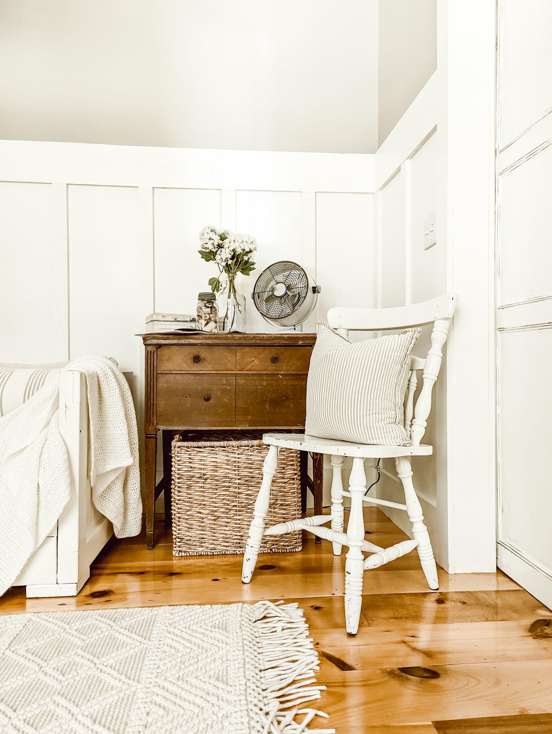 farmhouse cottage sitting area with white board and batten walls, chippy white furniture, and a wooden sewing cabinet as a side table