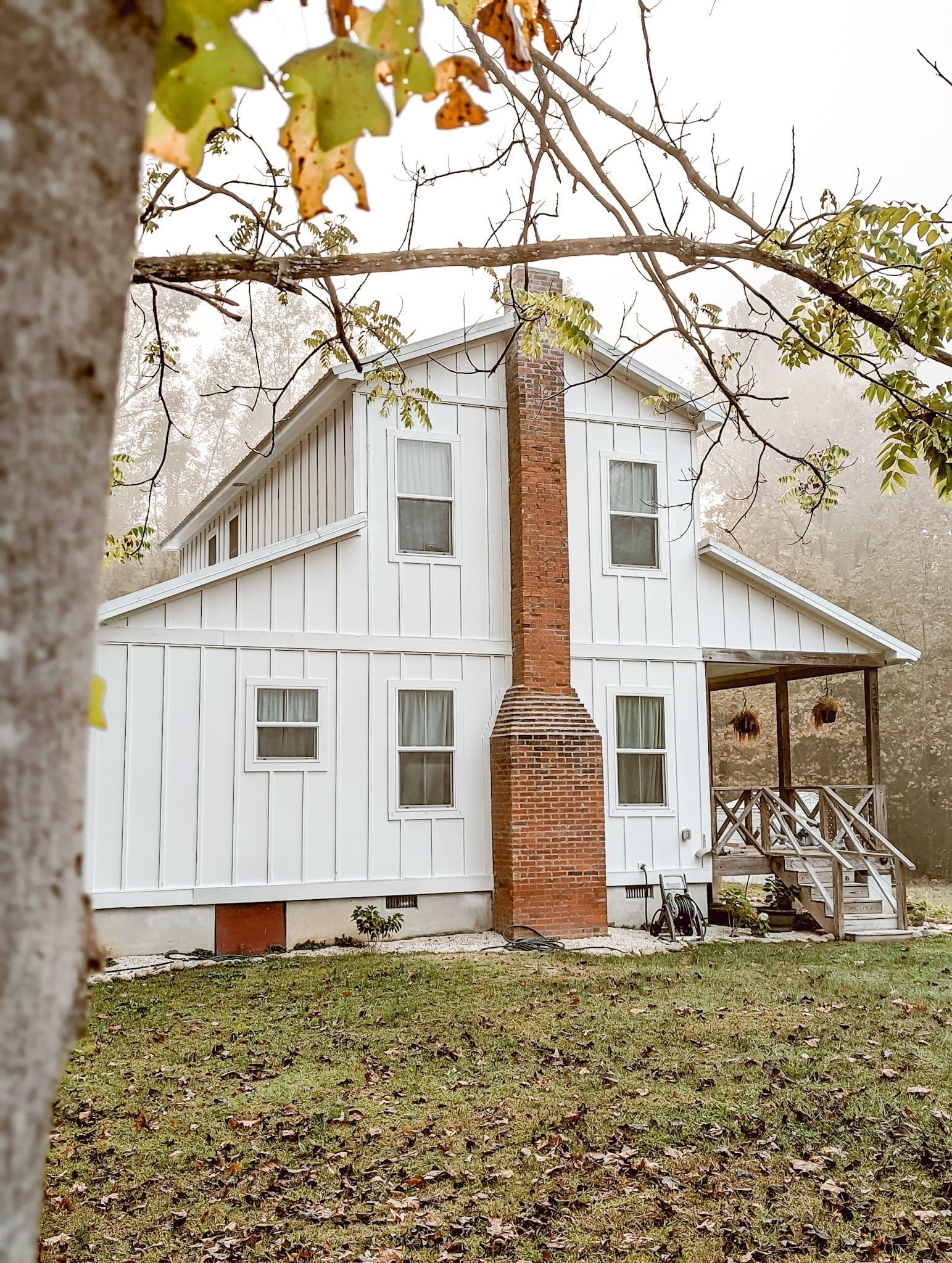 white farmhouse exterior with board and batten siding and a red brick chimney