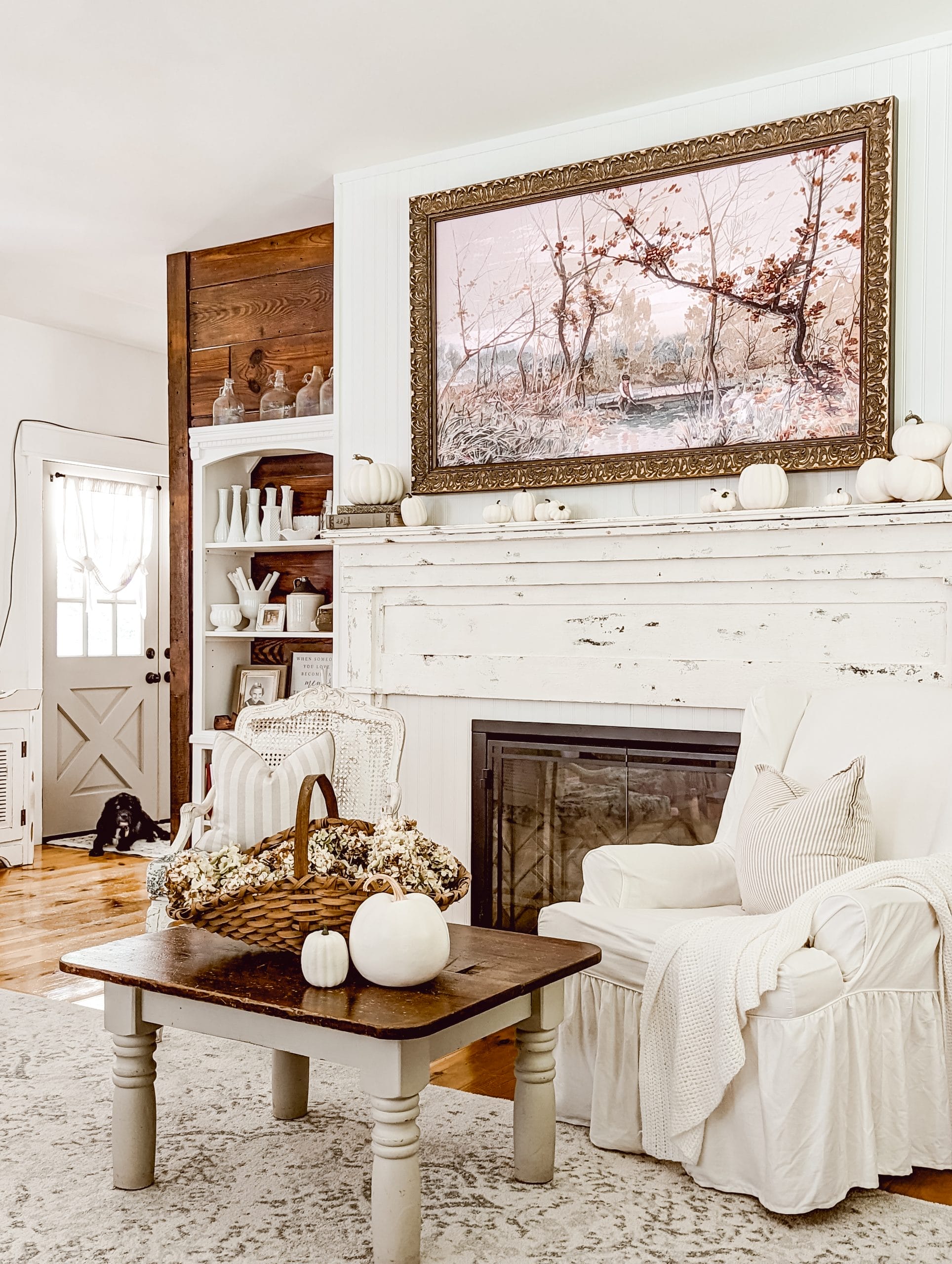 white and wood farmhouse living room with an antique mantel, an electric fireplace insert, and a Samsung Frame TV above the mantel