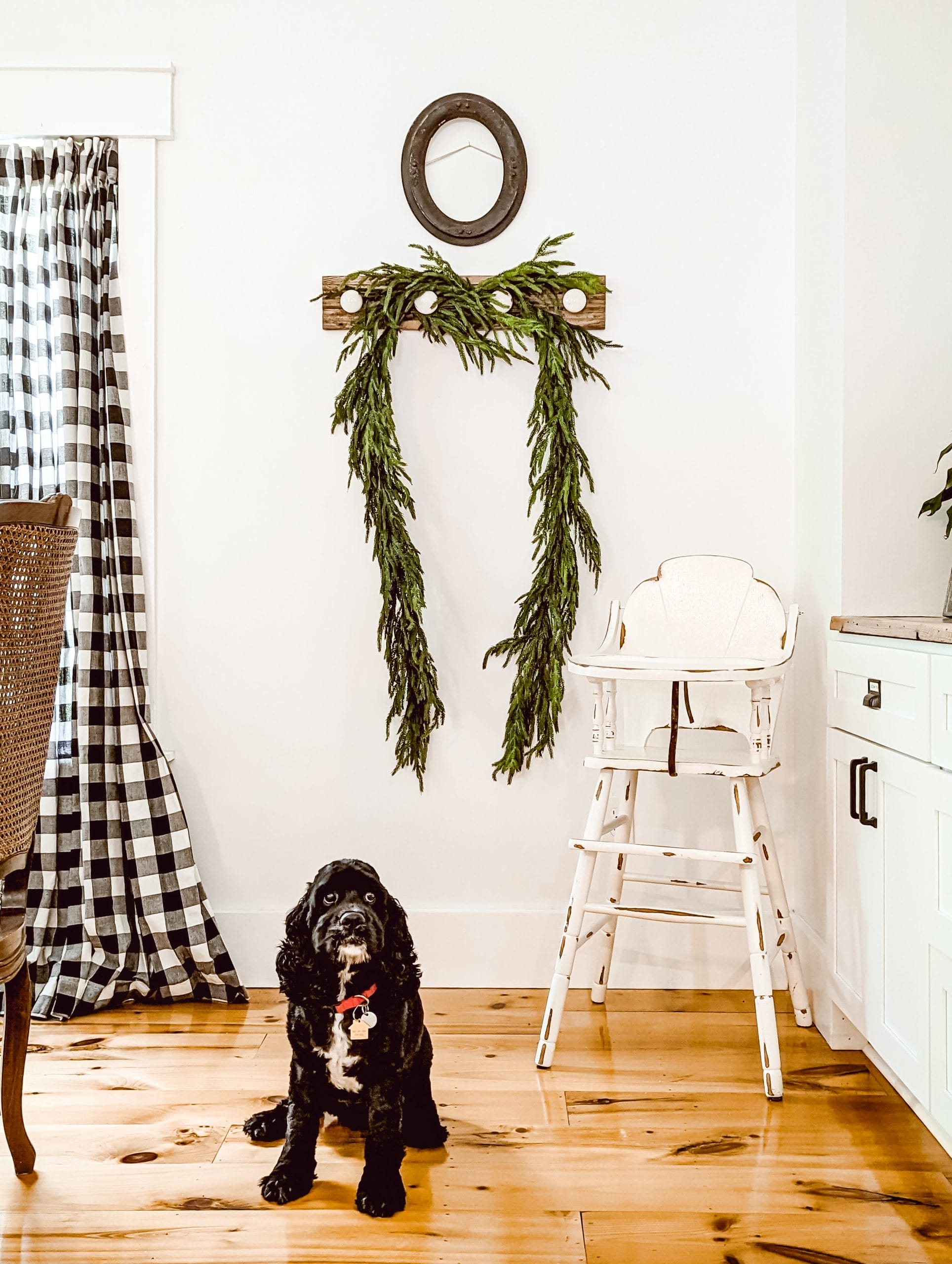 realistic Christmas greenery garland draped over hanging hooks in a white farmhouse dining room with a black cocker spaniel puppy