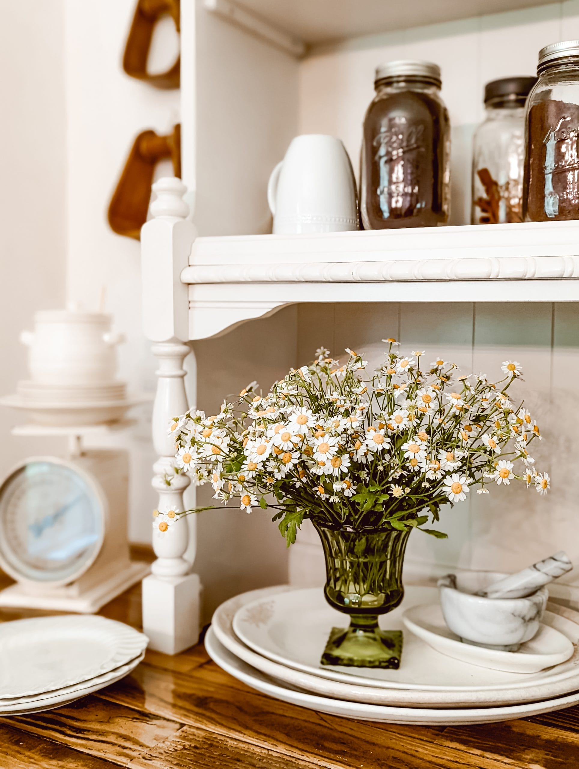 pretty white and yellow mini daisies arranged in a vintage green glass vase set on top of a stack of thrifted antique white platters