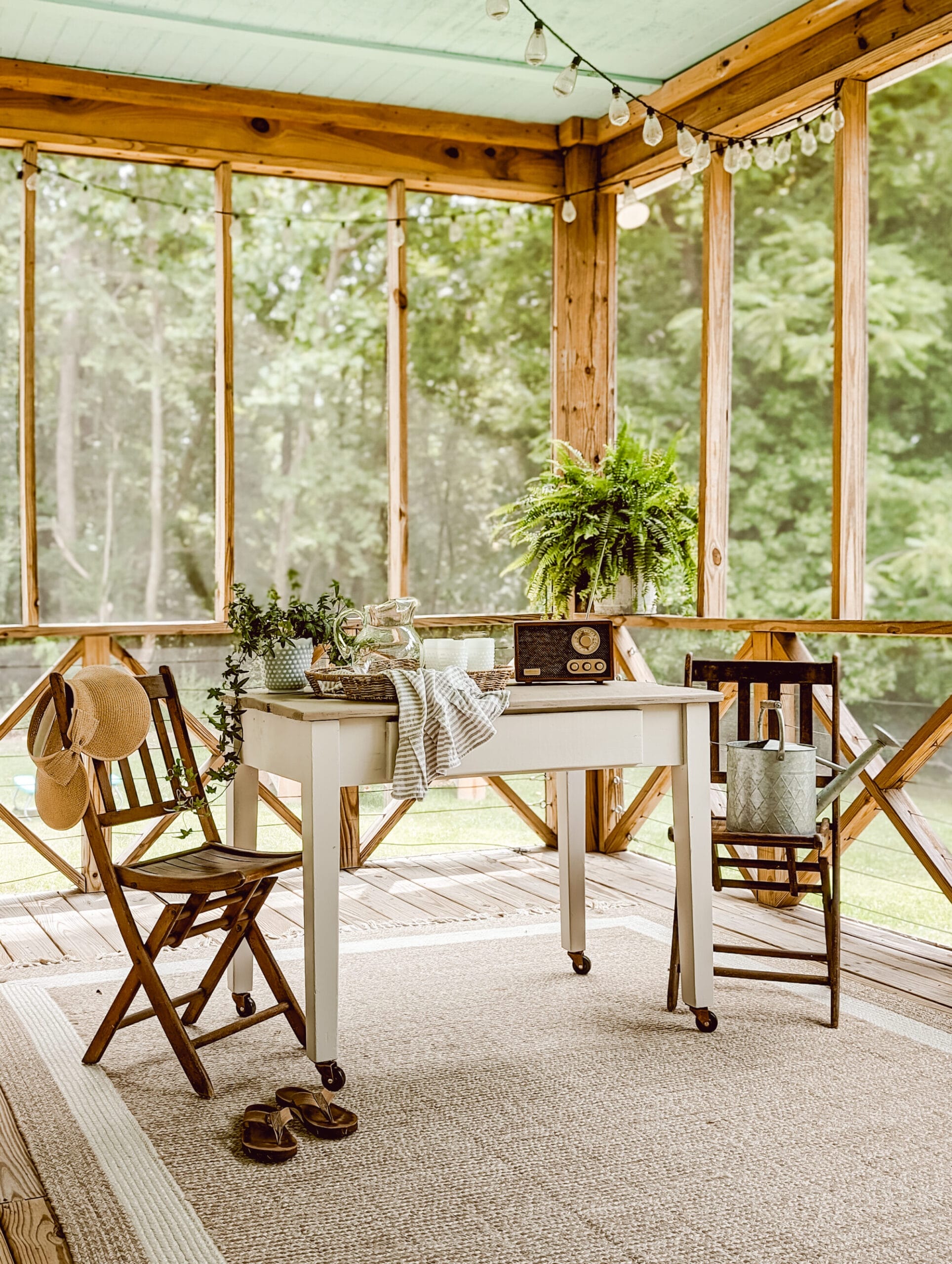 farmhouse style screened in porch with rolling table and two vintage wood folding chairs on a beige outdoor rug