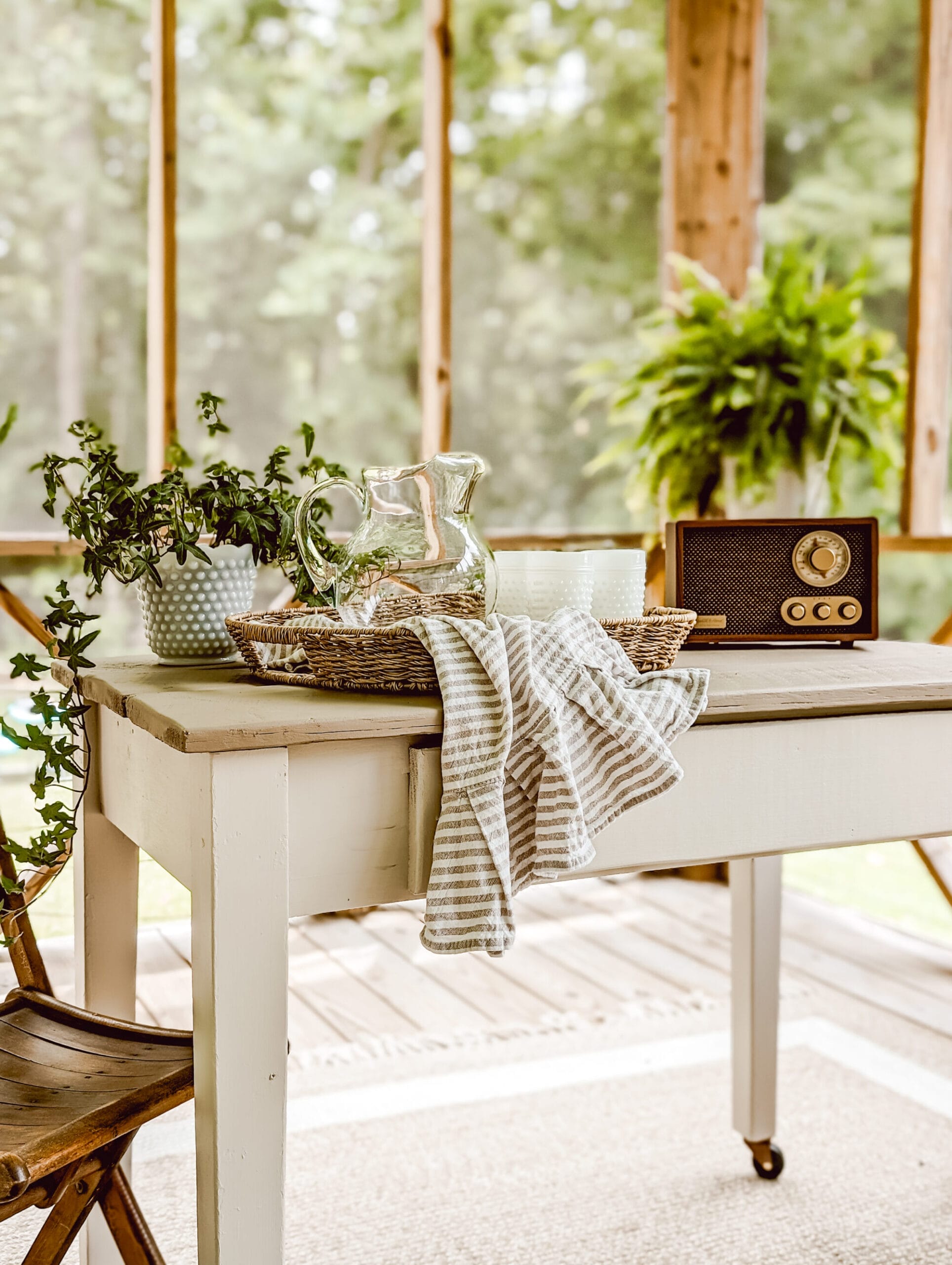 wicker tray on a painted table holding a drink pitcher and vintage milk glass drinking glasses and a striped tea towel