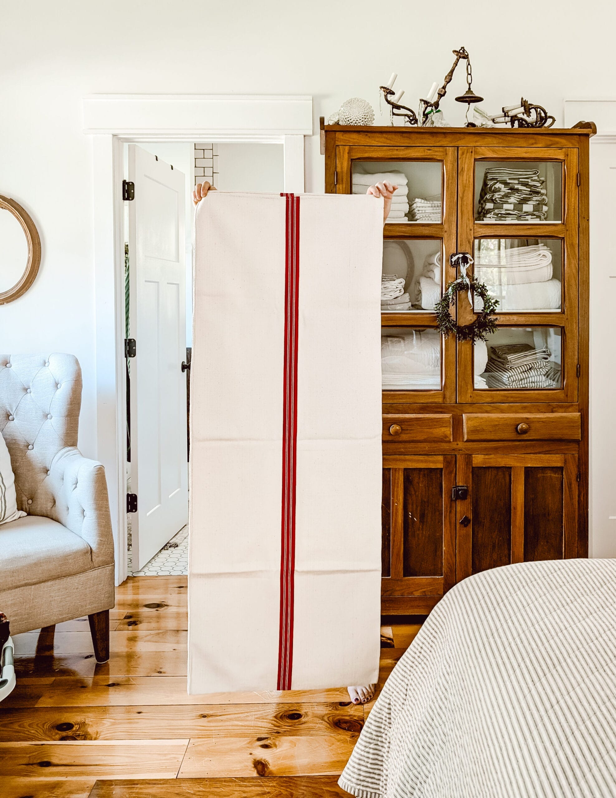 holding up an antique red striped grain sack in front of our farmhouse linen cabinet