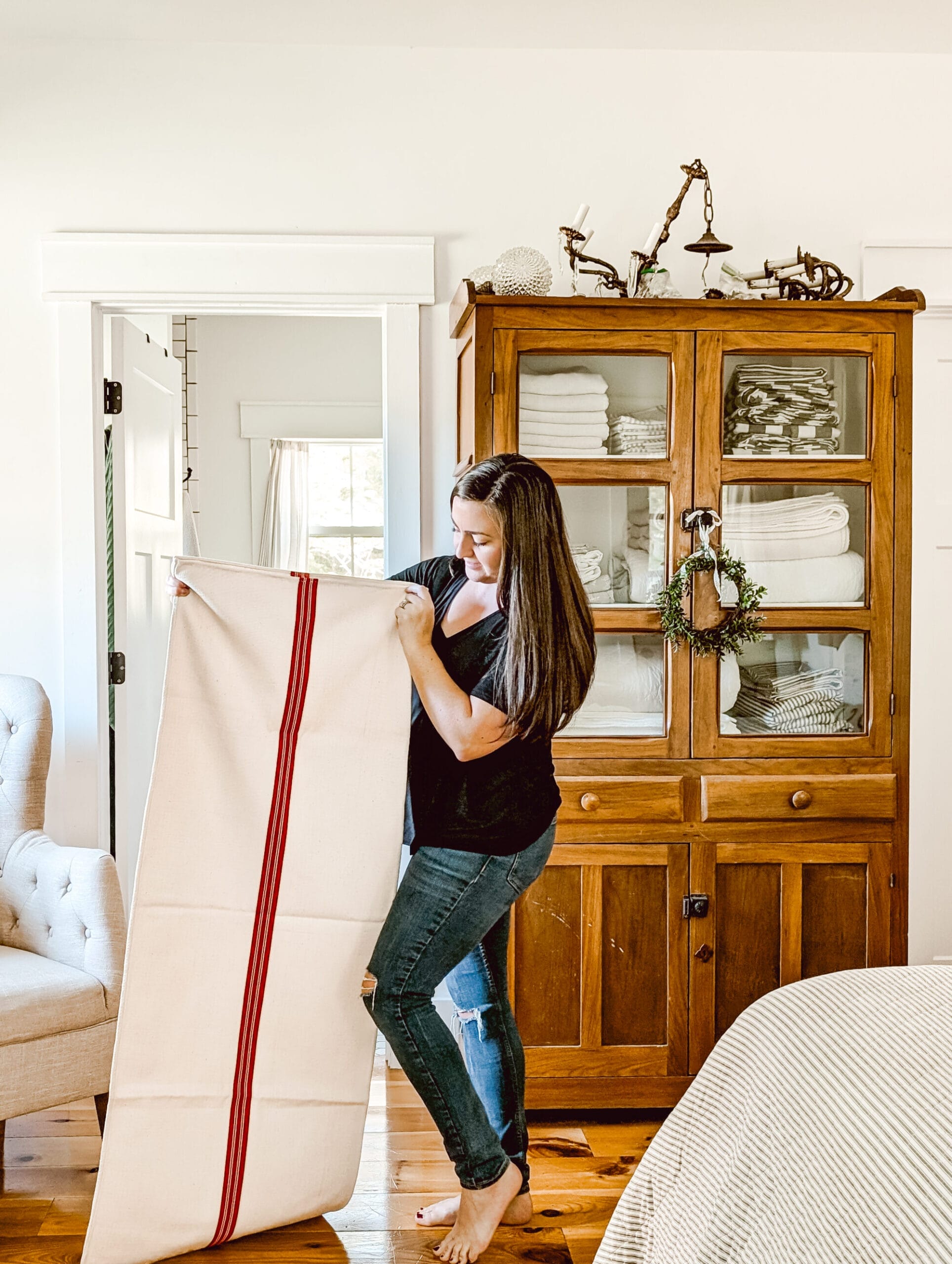 holding up an antique red striped grain sack in front of our farmhouse linen cabinet