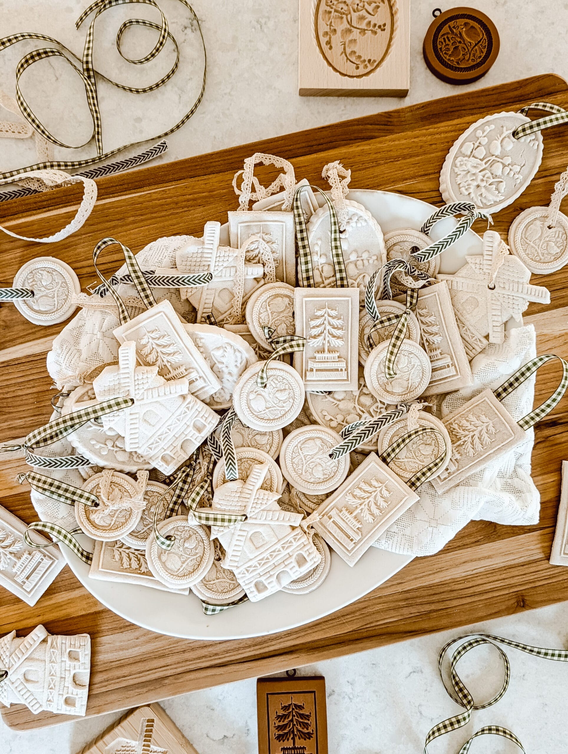 fancy heirloom style DIY salt dough Christmas ornaments on a white platter stacked on a wood cutting board