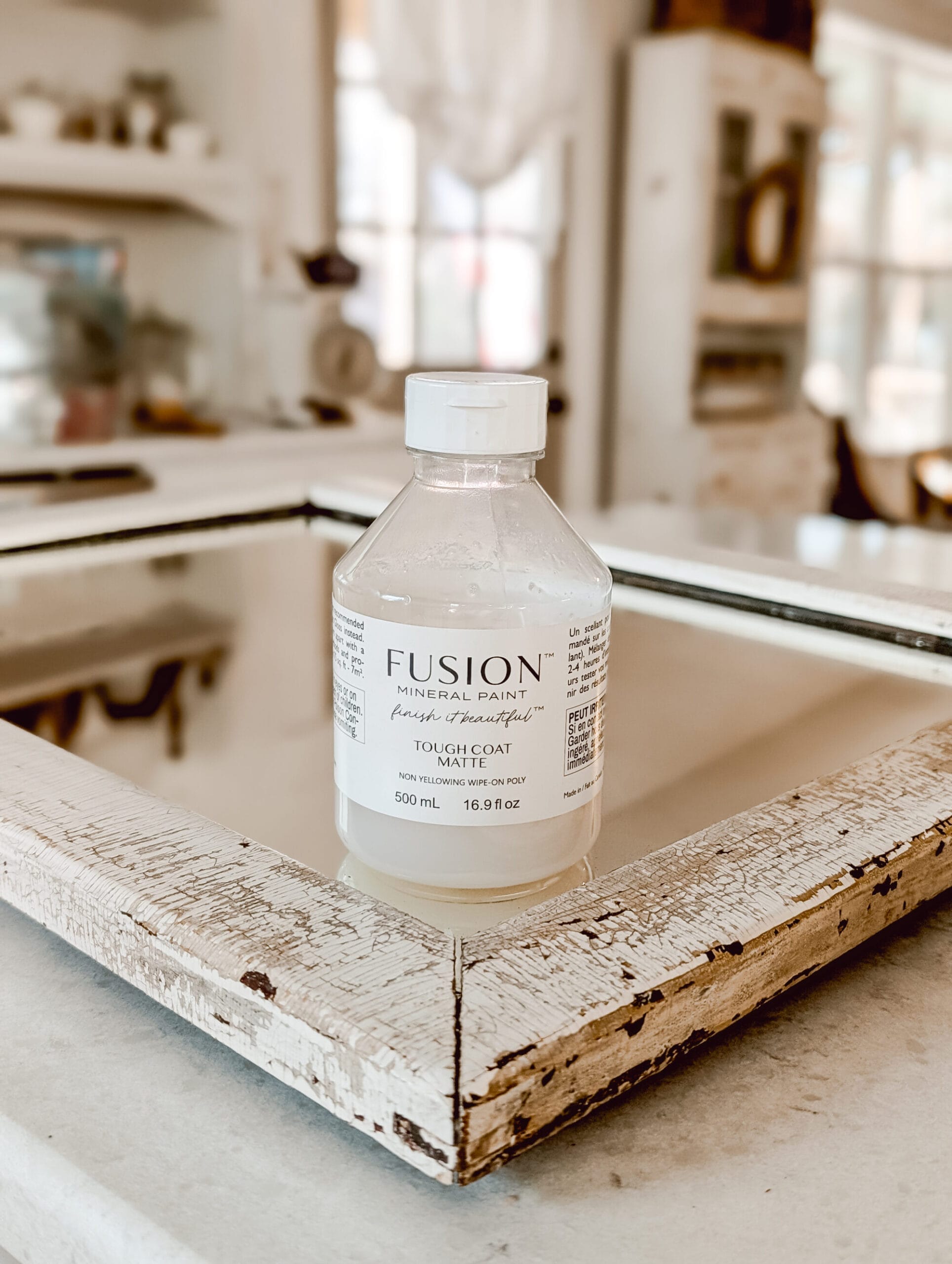 Bottle of Tough Coat non yellowing poly by Fusion Mineral Paint sitting on a chippy antique mirror