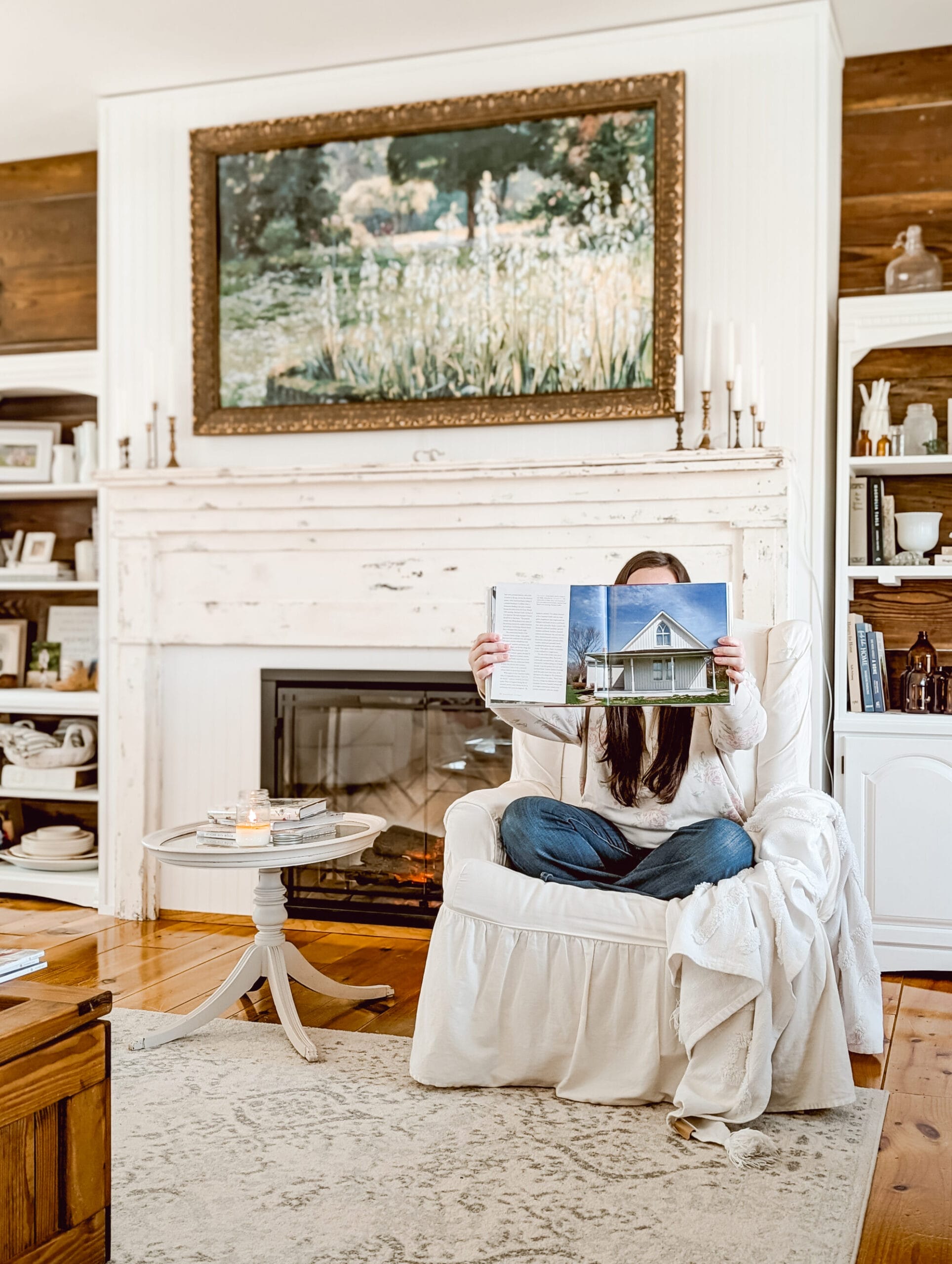 holding up a book with the American Gothic House inside of our white cottage farmhouse style living room and fireplace