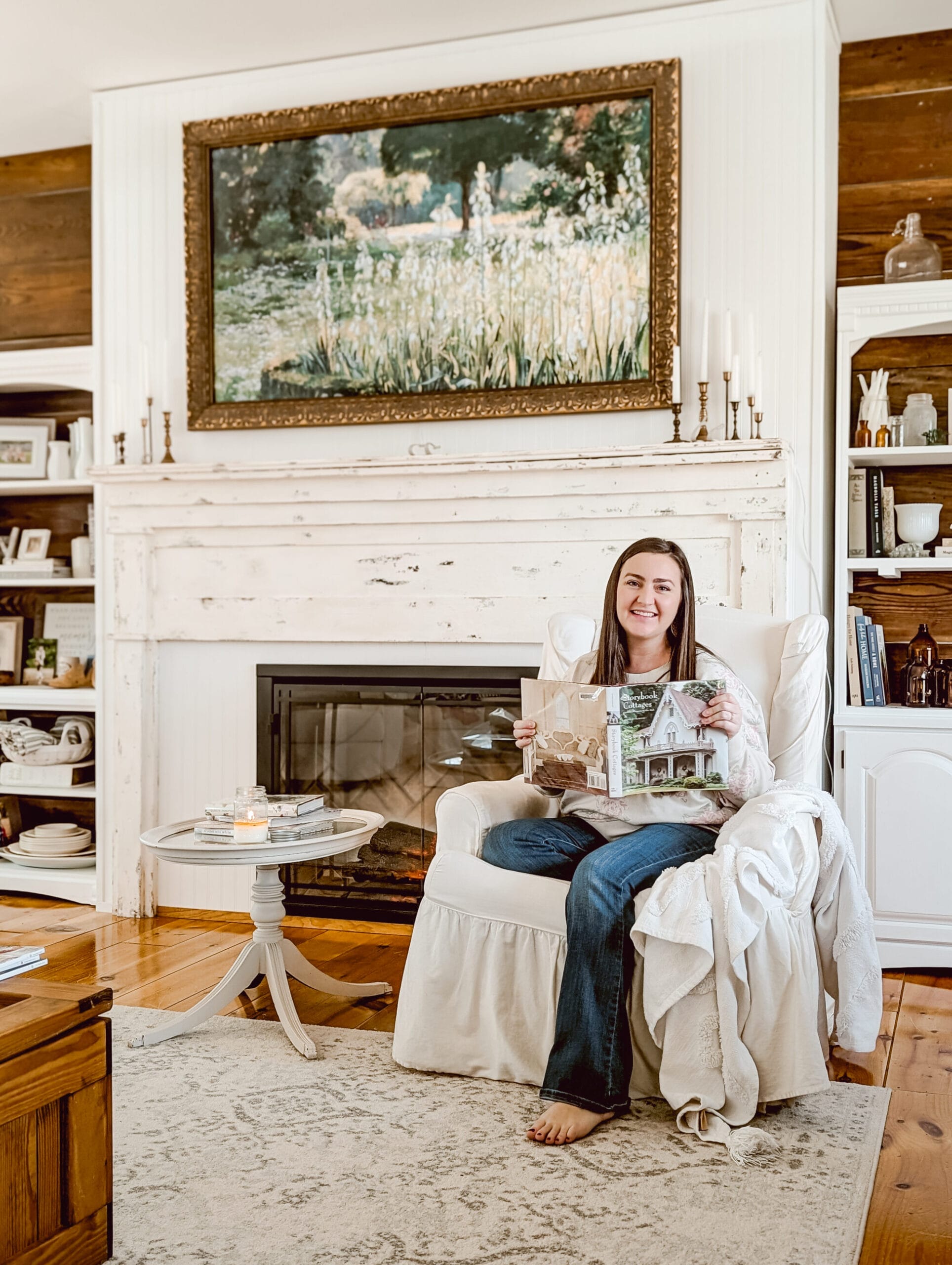 sitting in a wing back rocking chair reading "Storybook Cottages" for interior design inspo in a white farmhouse style living room