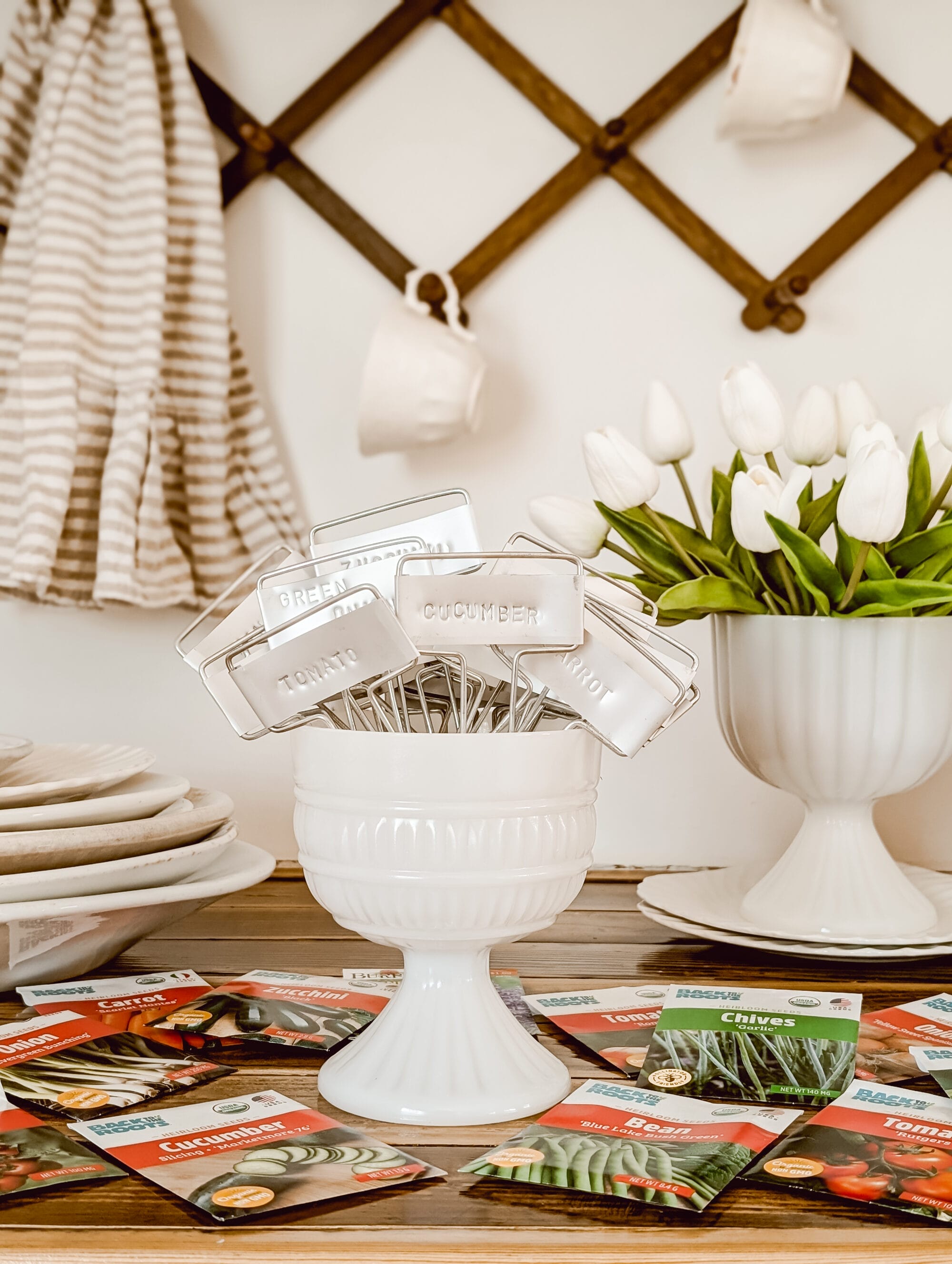 stamped metal plant markers arranged in a vintage milk glass pedestal planter on a wood countertop 