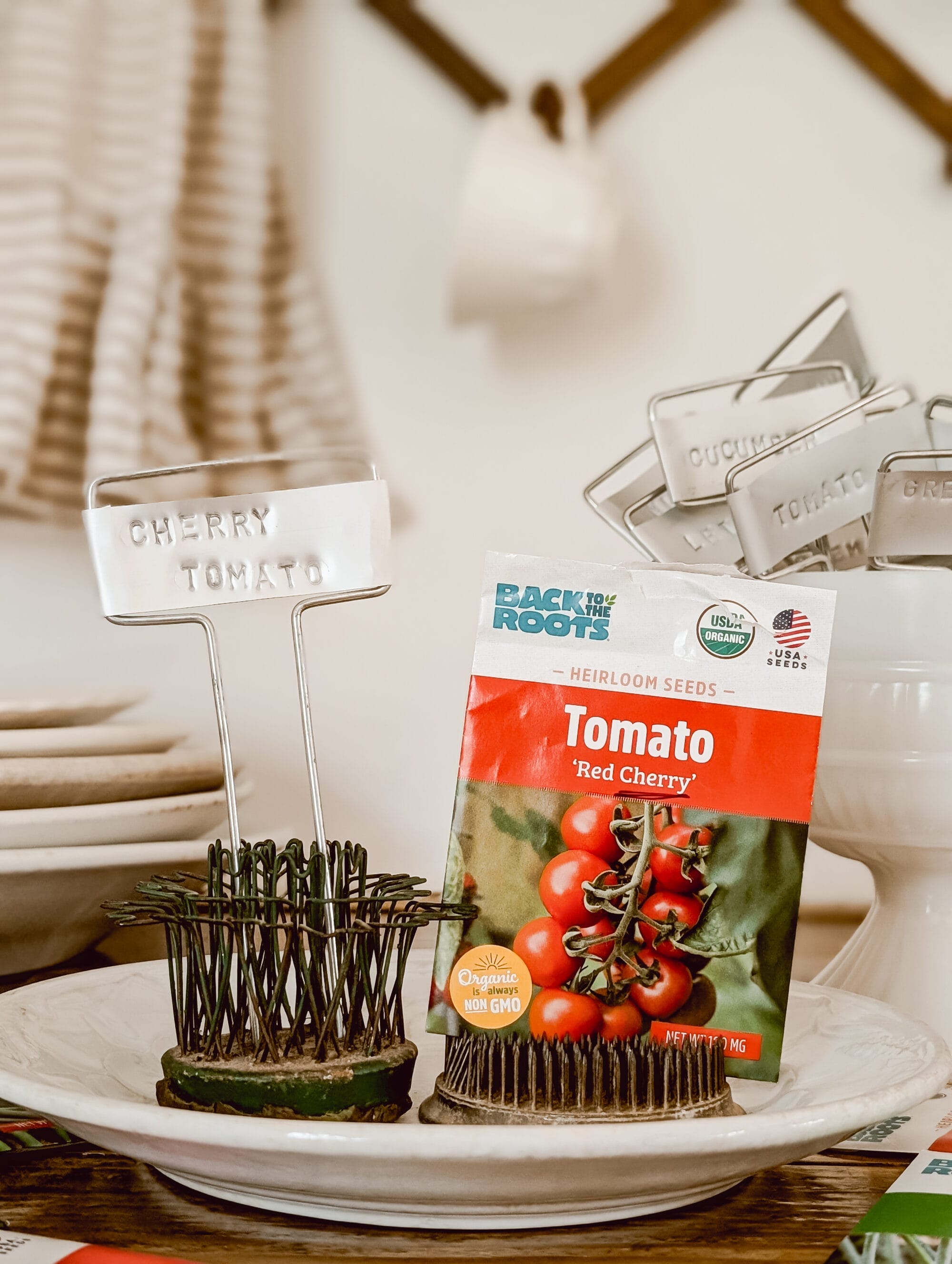 metal plant marker with "cherry tomato" stamped into the label and a pack of cherry tomato seeds displayed in vintage flower frogs