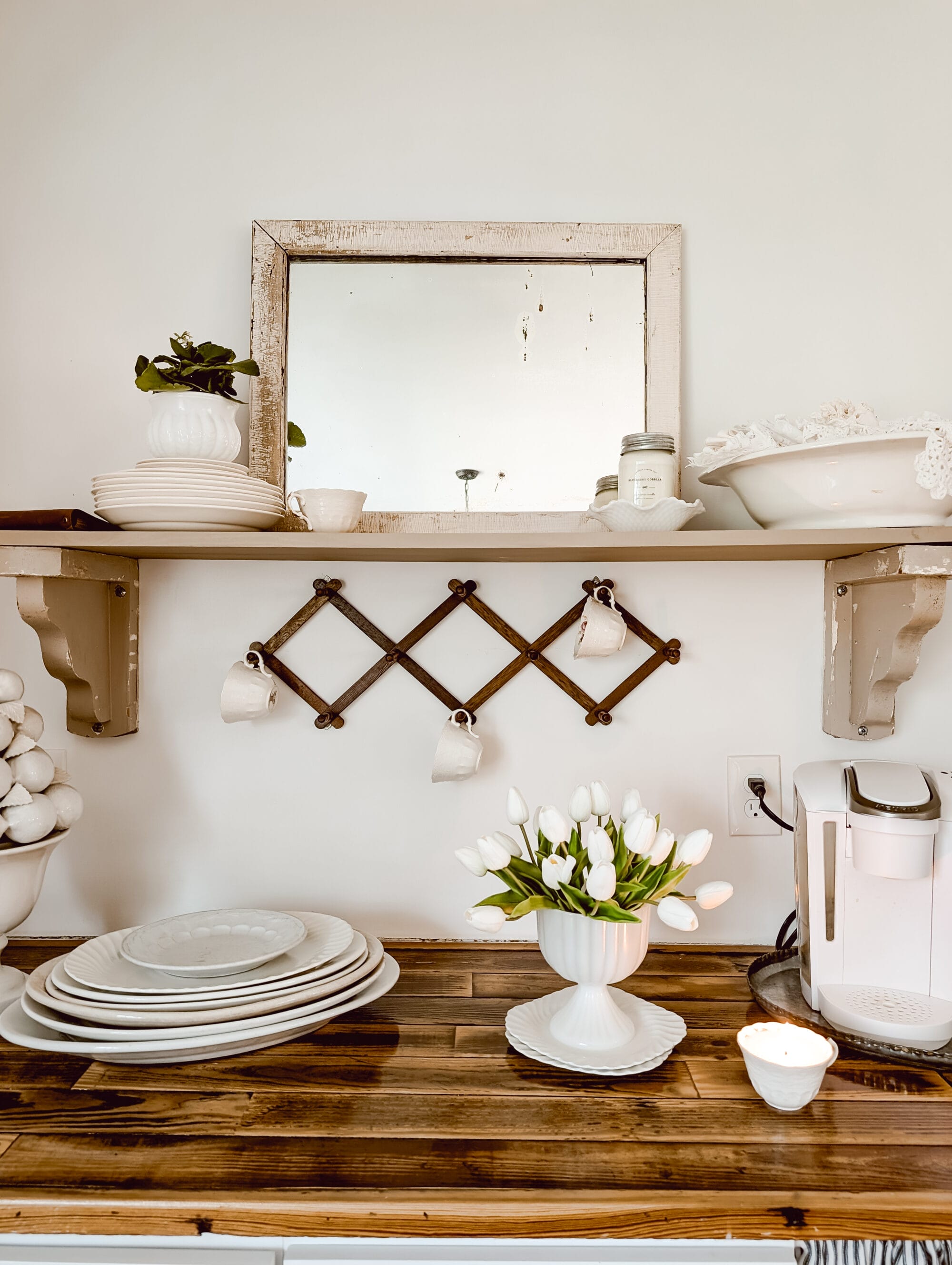 simple cottage style built-in coffee bar with open shelving, vintage dishes, and white tulips arranged in a milk glass pedestal planter