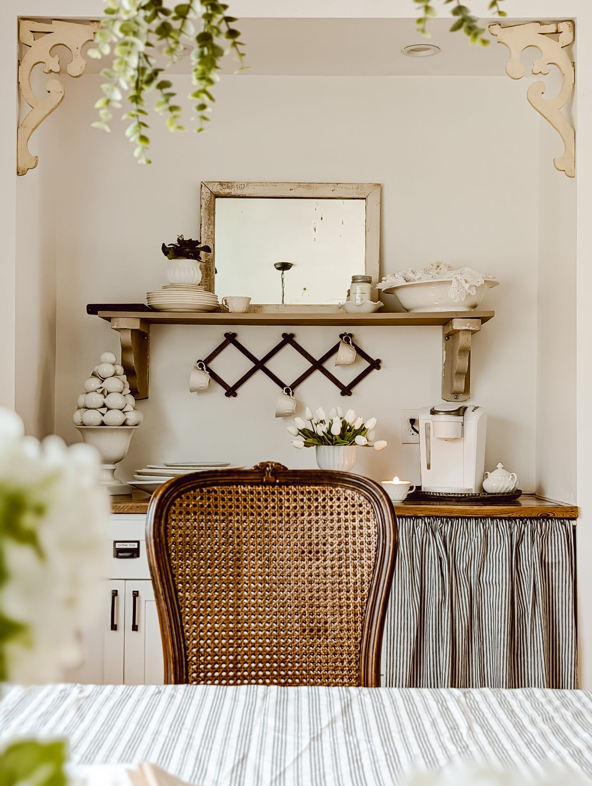 simple cottage style built-in coffee bar with open shelving, vintage dishes, and white tulips arranged in a milk glass pedestal planter
