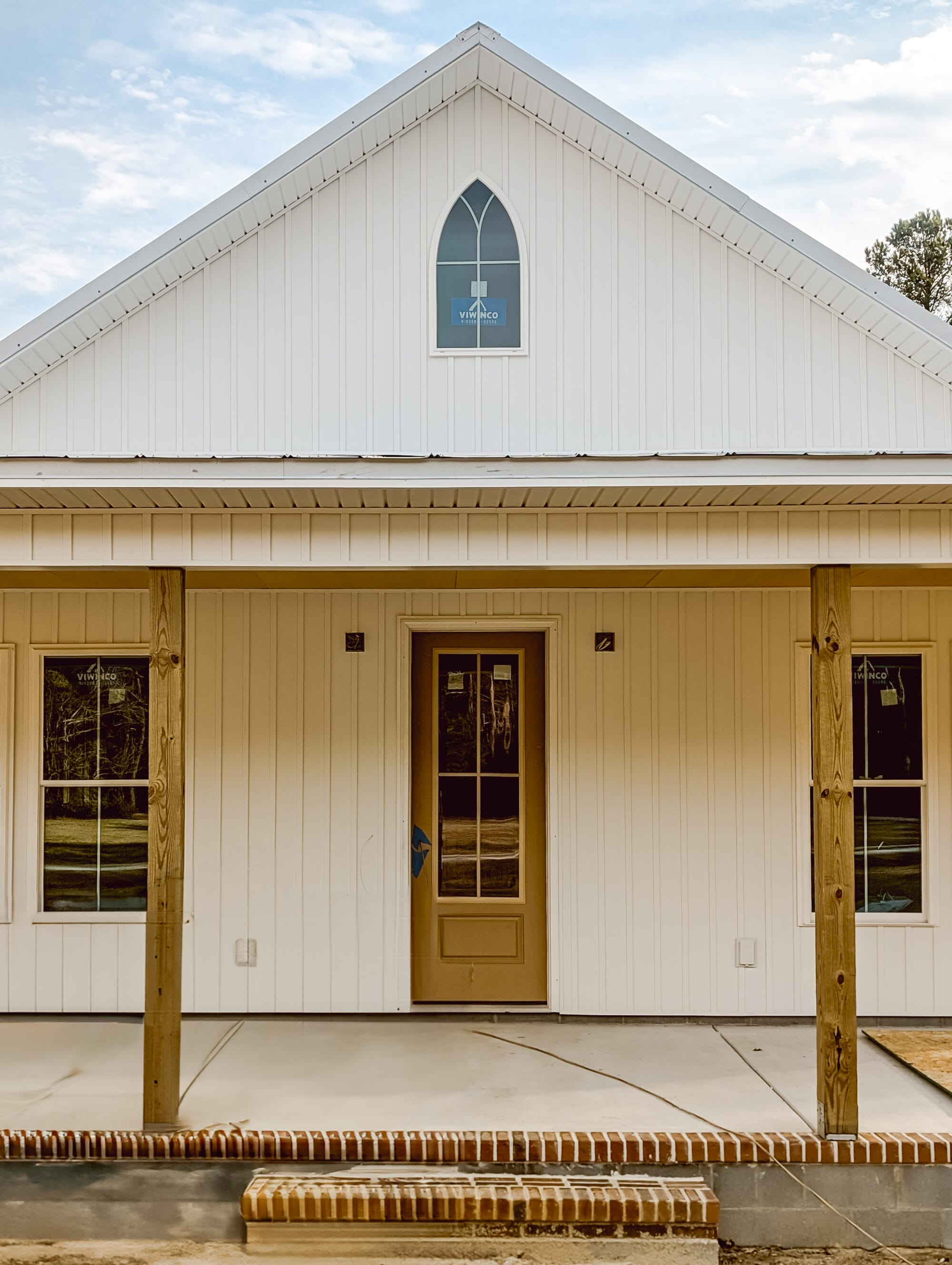 arched window in the attic on a white cottage with board and batten siding
