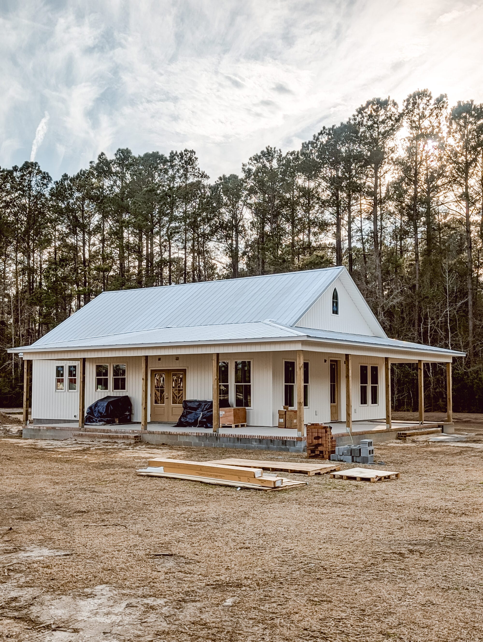 cottage with white board and batten siding, a metal roof and an arched church window under construction