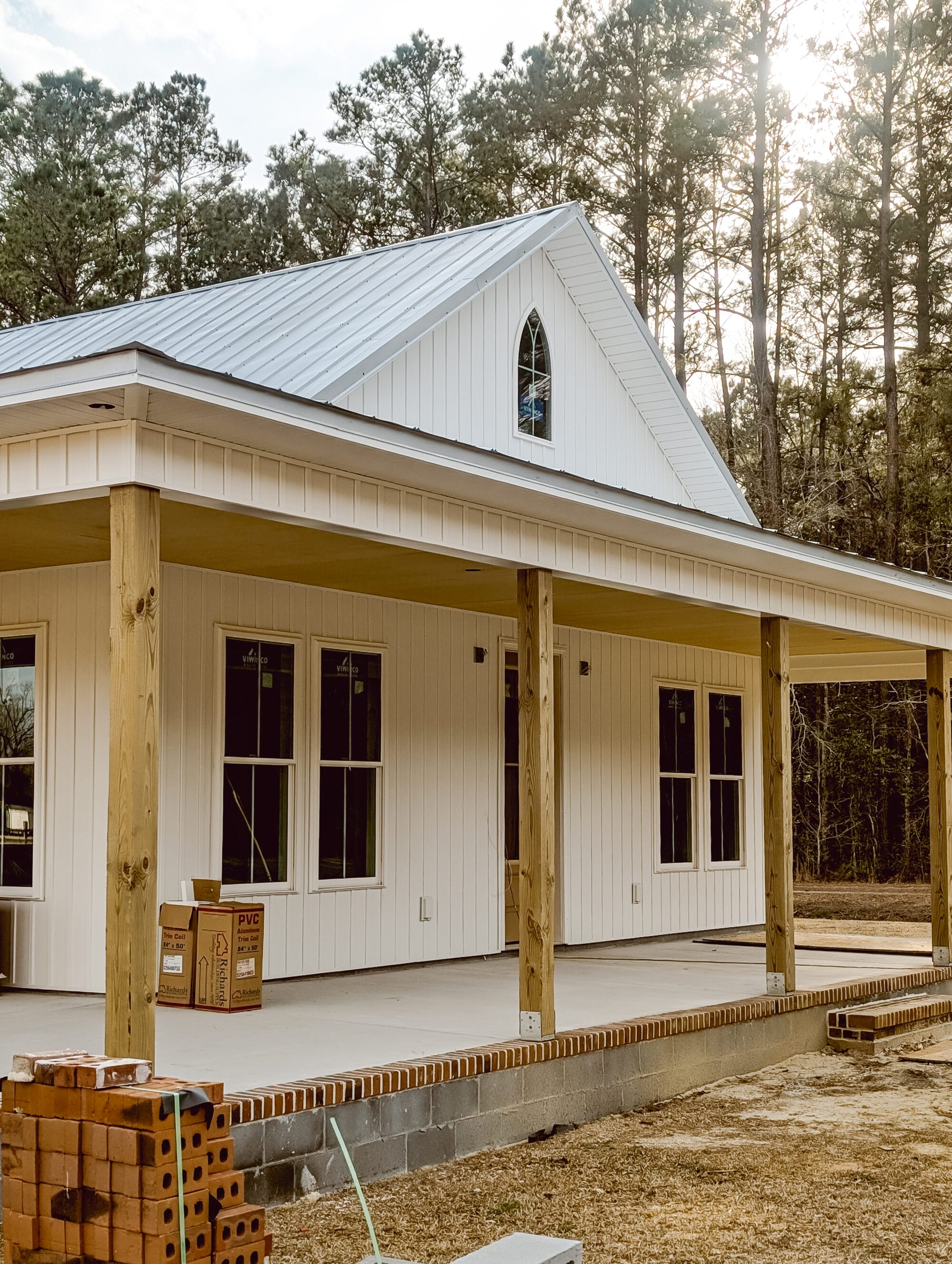 Carpenter Gothic inspired cottage with white board and batten siding, a metal roof and an arched church window