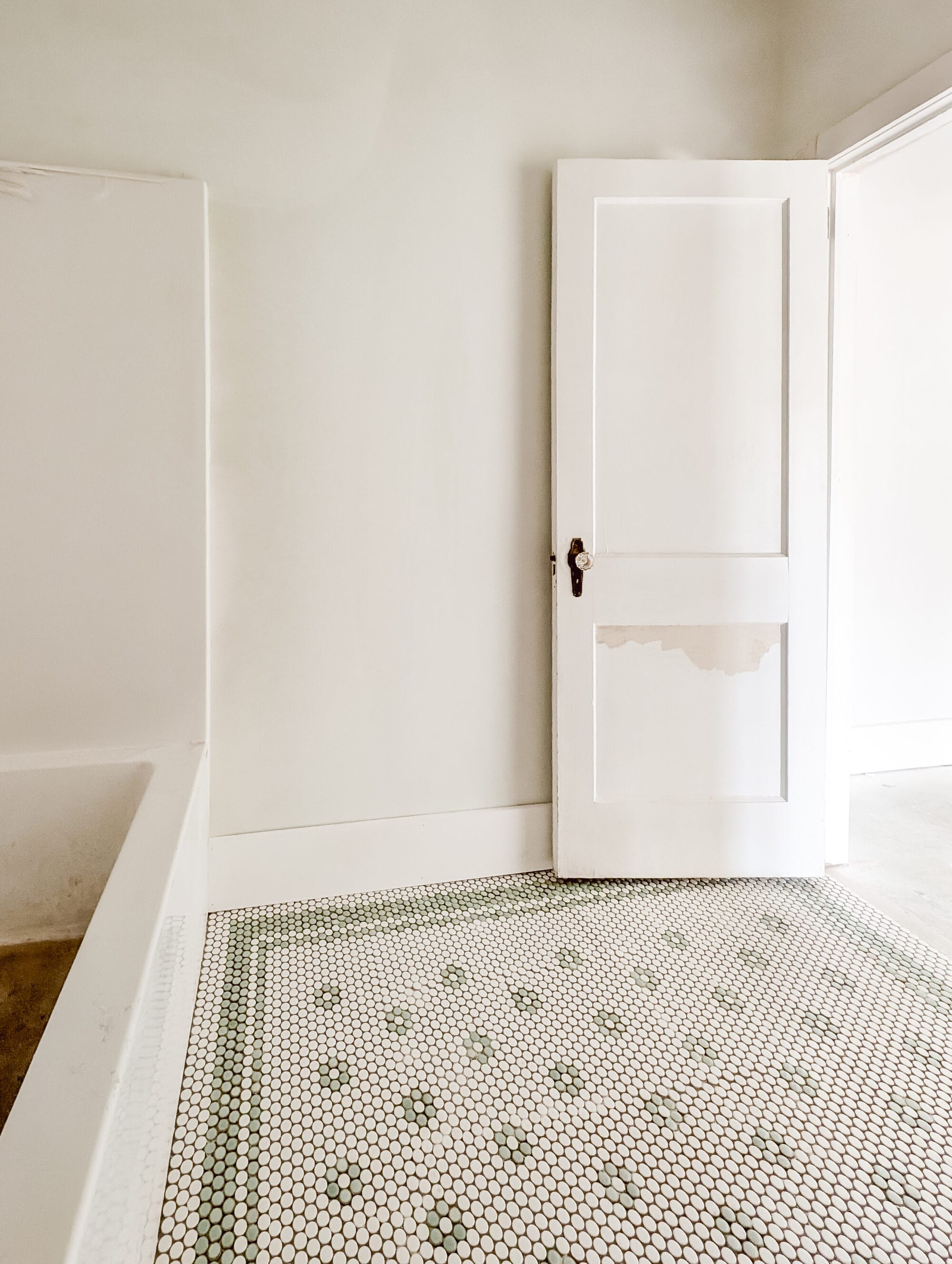 vintage cottage guest bathroom progress with mint green and white penny tile in a daisy pattern and an antique door with brass and crystal knob