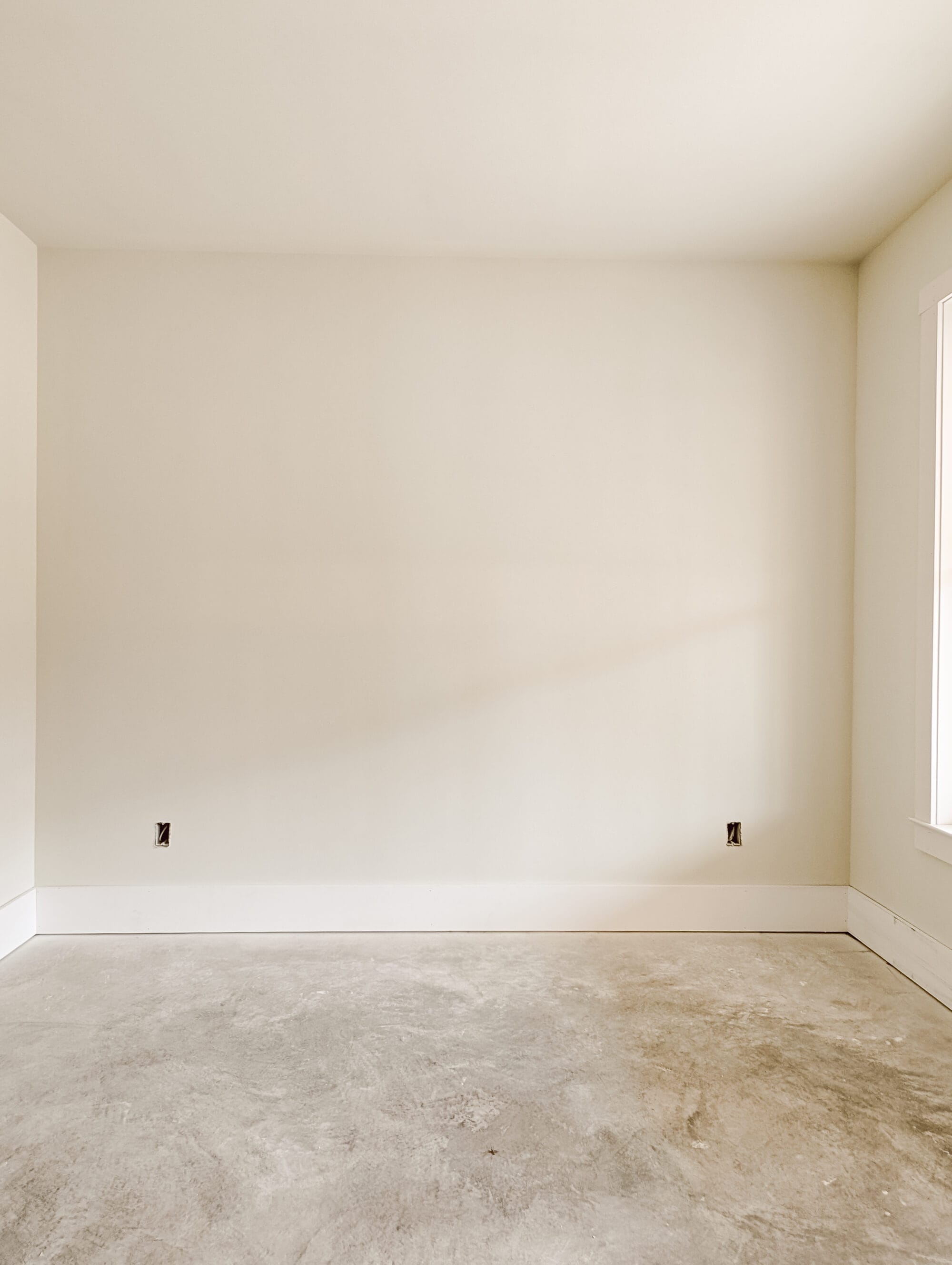 bed wall in our unfinished cottage guest bedroom with primed walls and concrete subfloors