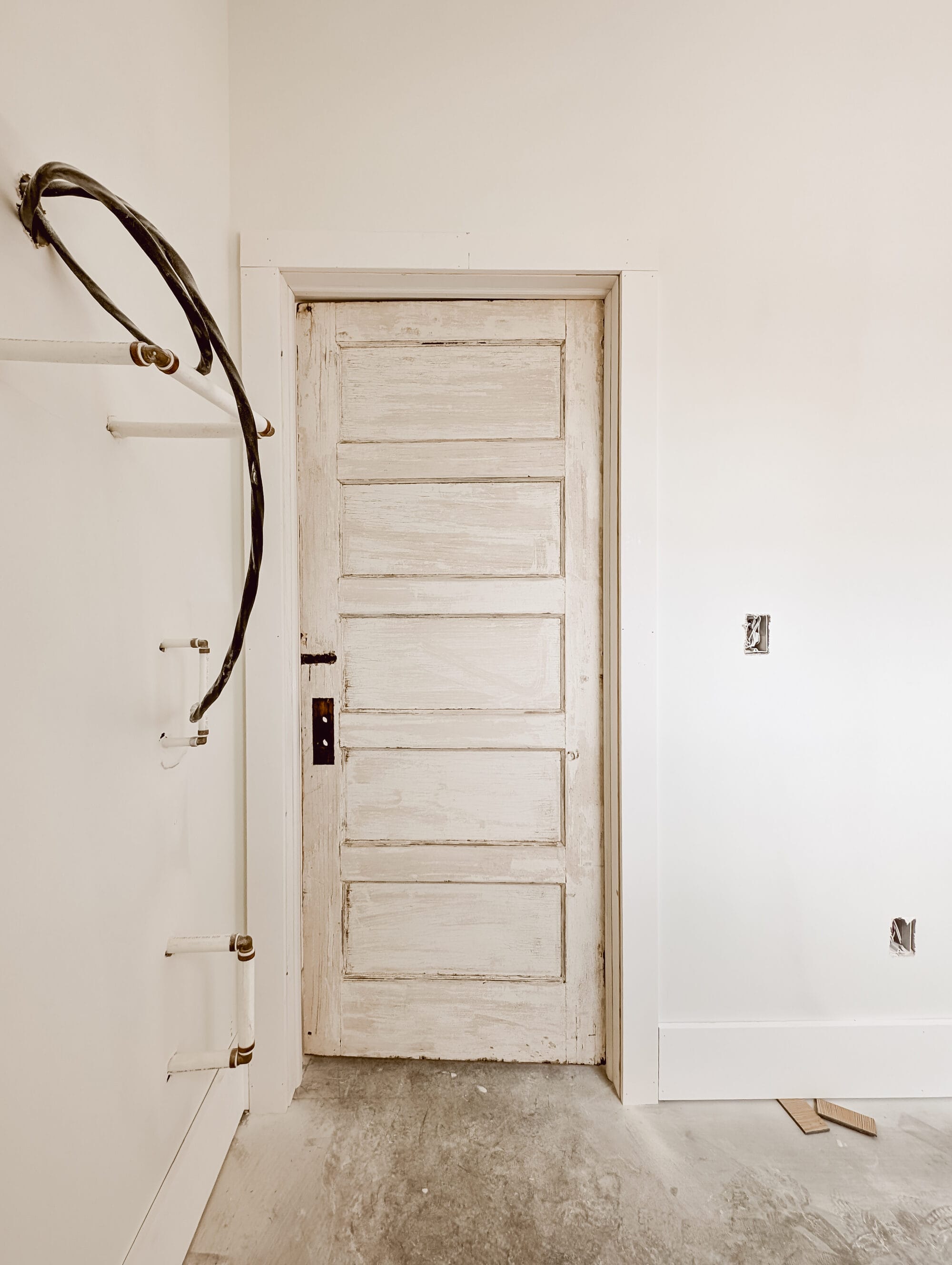 salvaged 5 panel door inside our unfinished laundry room with concrete subfloors and primed walls