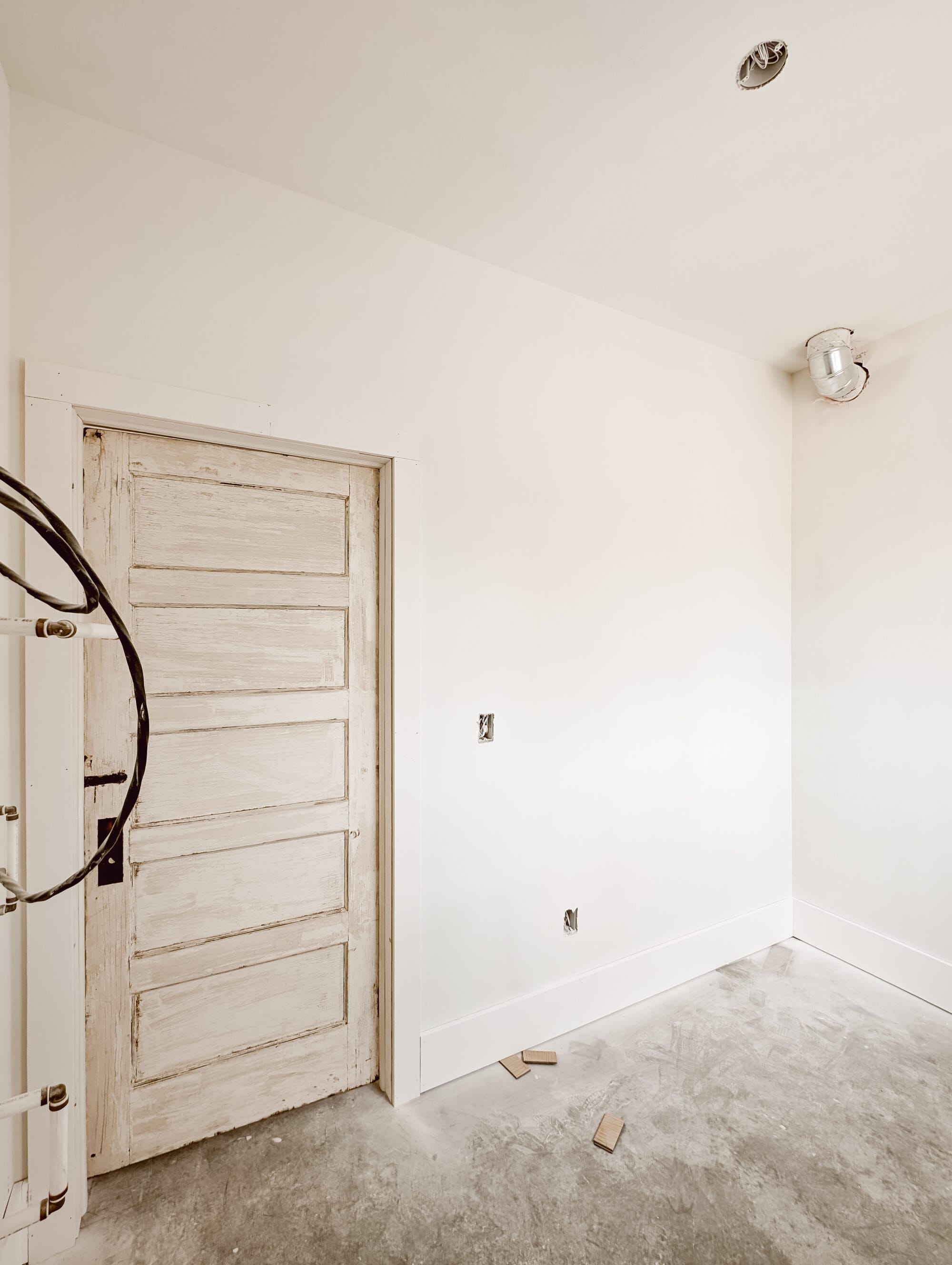 salvaged 5 panel door inside our unfinished laundry room with concrete subfloors and primed walls