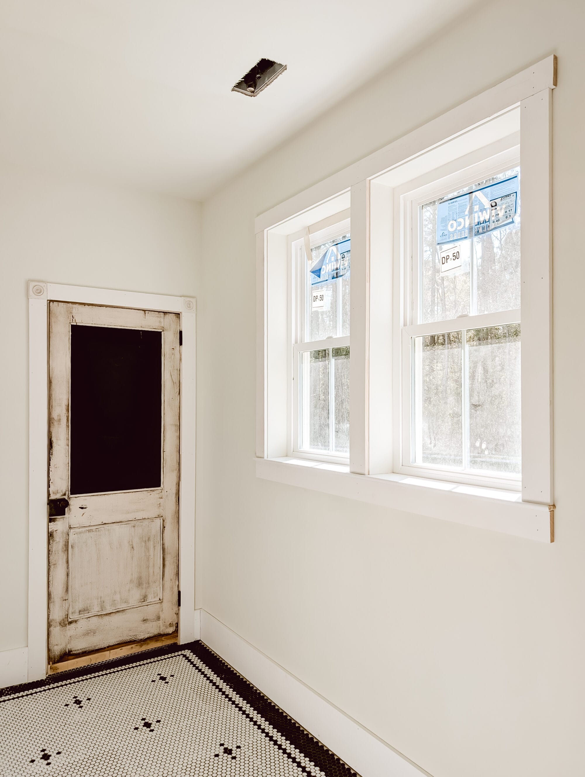 new old cottage bathroom with black and white penny tile floors, and antique door and a double window