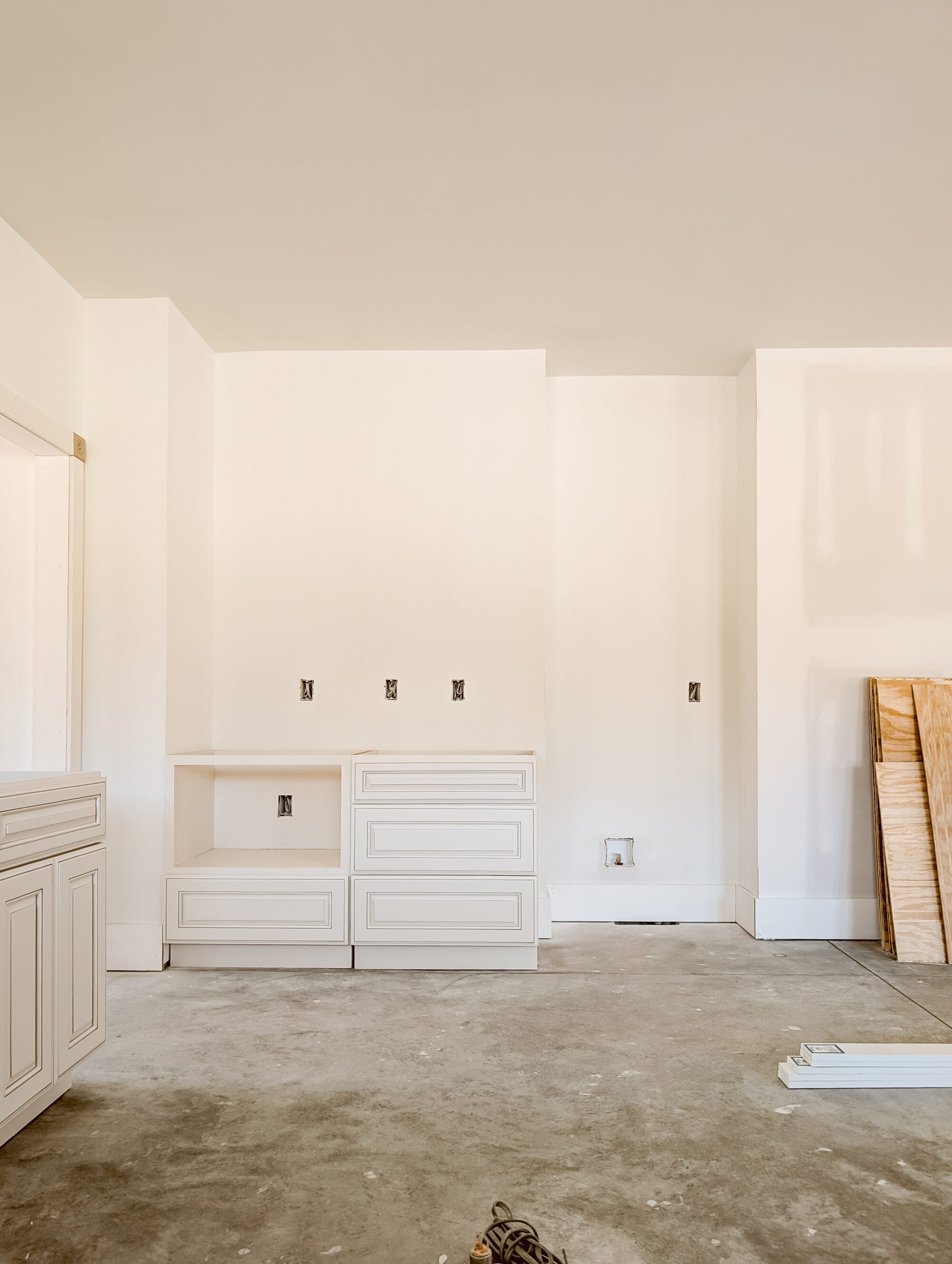 unfinished new old cottage kitchen with new cabinets, concrete subfloor and primed walls, and a nook for the fridge