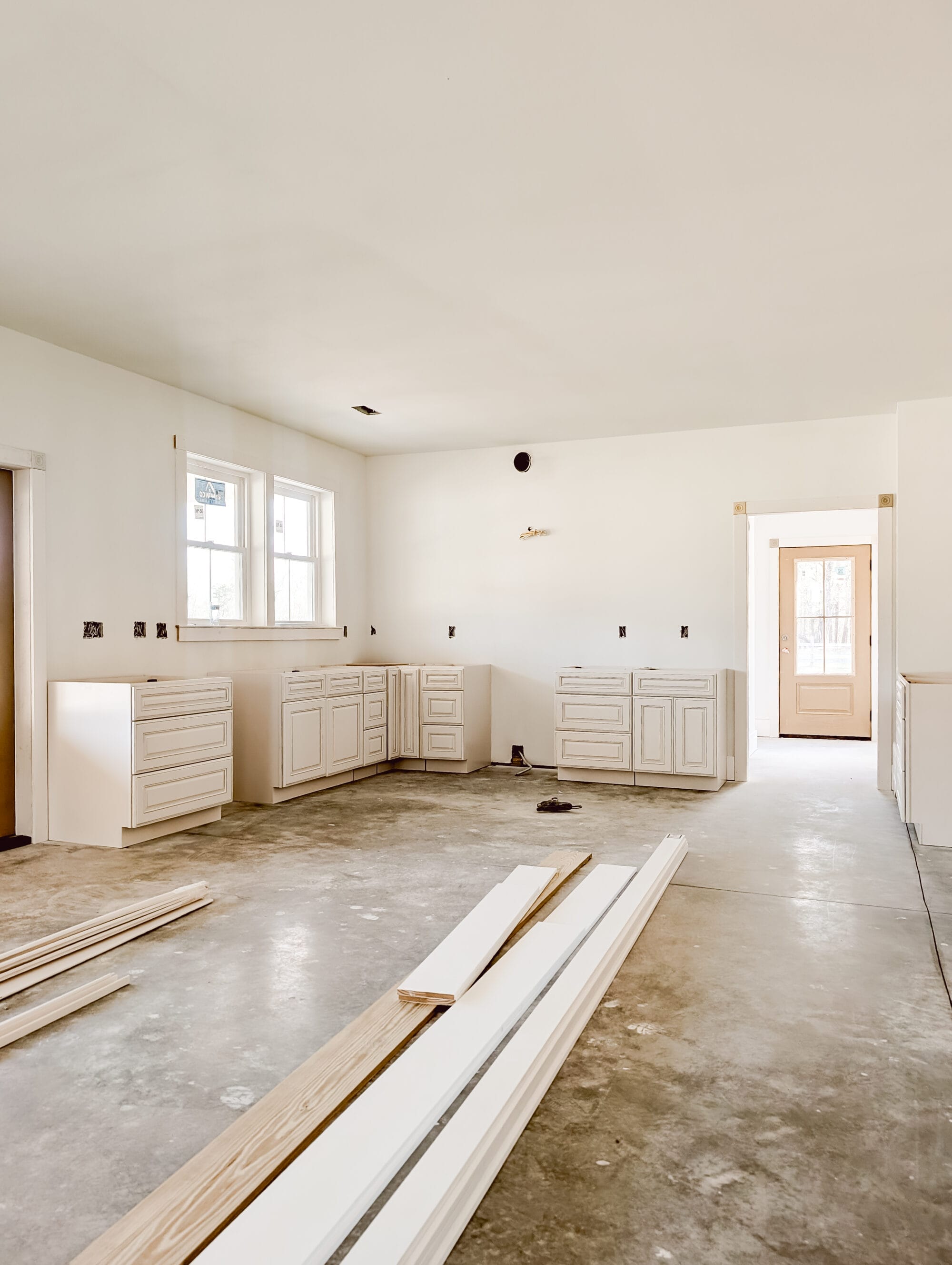 views inside our unfinished cottage kitchen with new cabinets, concrete subfloor and primed walls