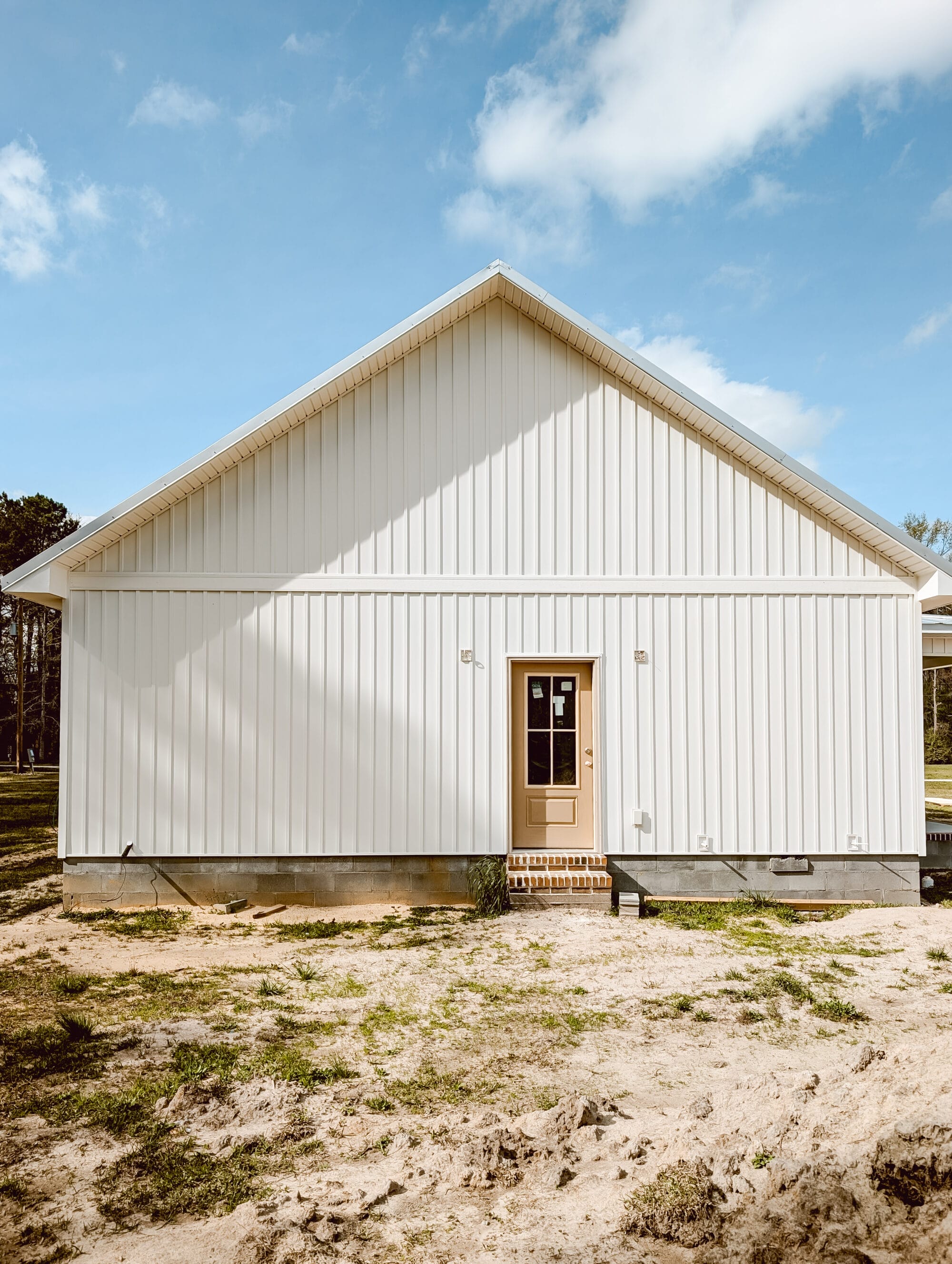 the back of our new old cottage still under construction with white board and batten siding and a 3/4 light glass back door