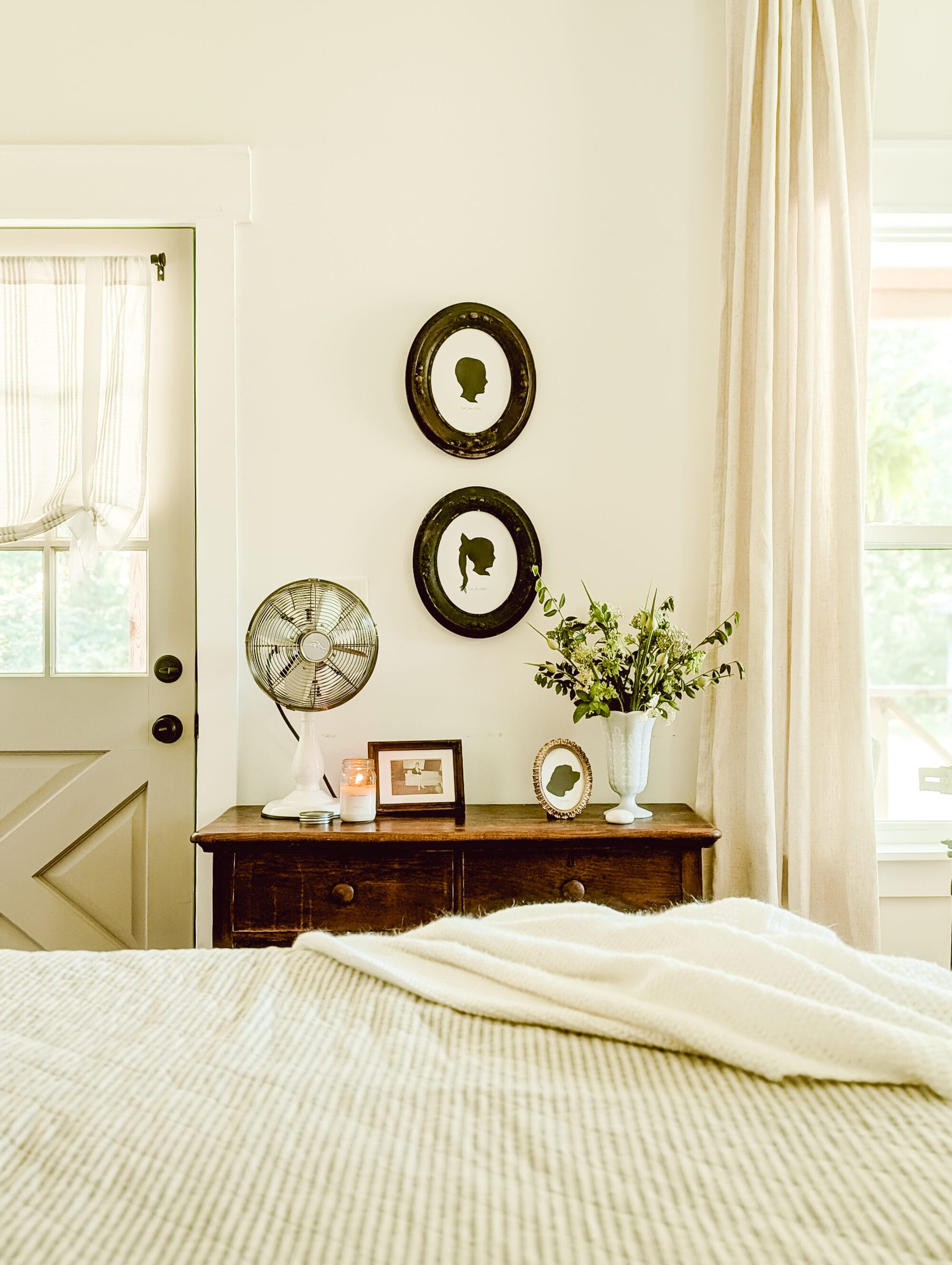 framed black and white silhouette portraits hung on the wall over an old wood dresser in a neutral farmhouse bedroom