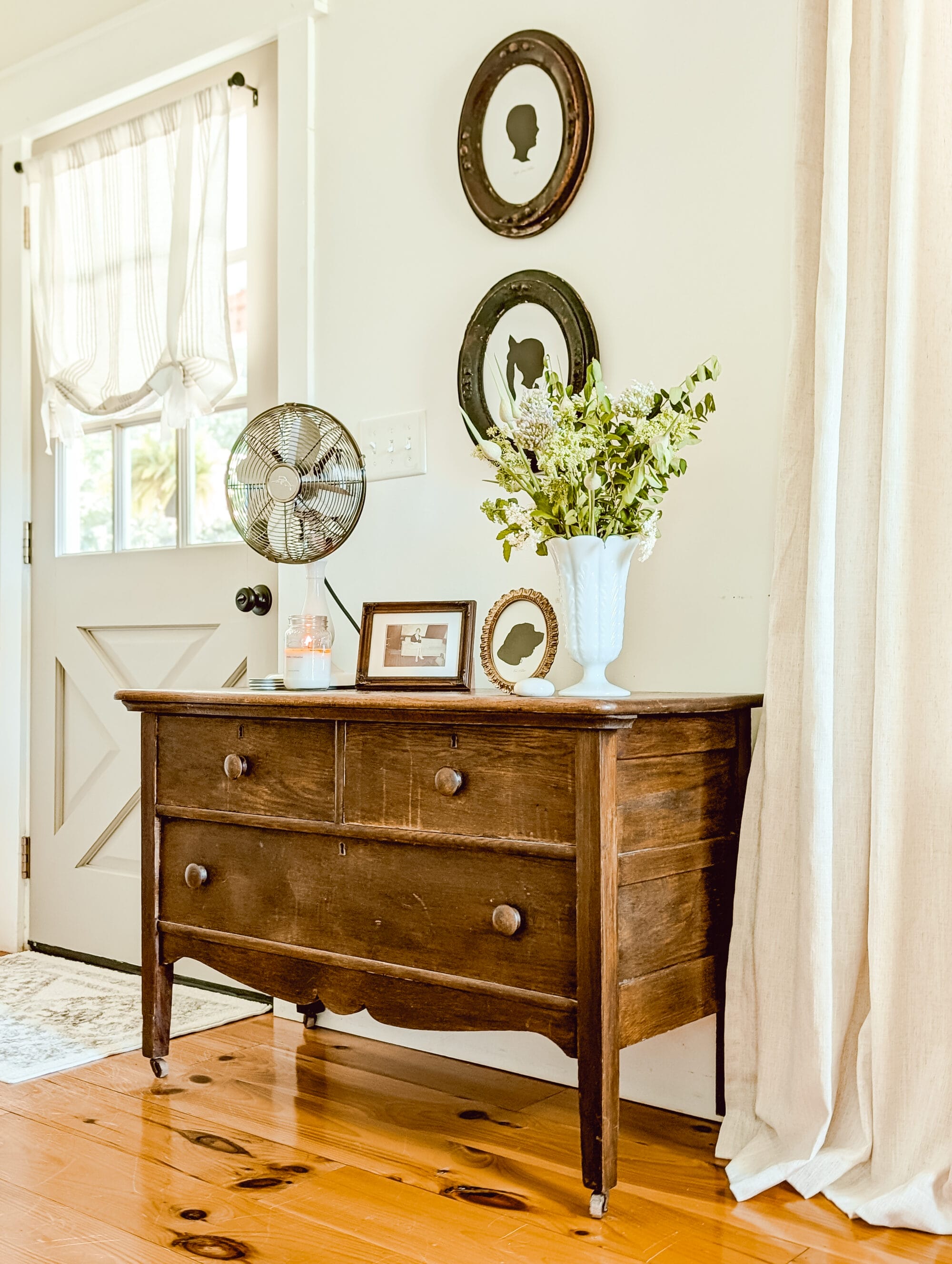 vintage wood 3-drawer dresser with vintage style fan on top of it and green florals in a white milk glass vase