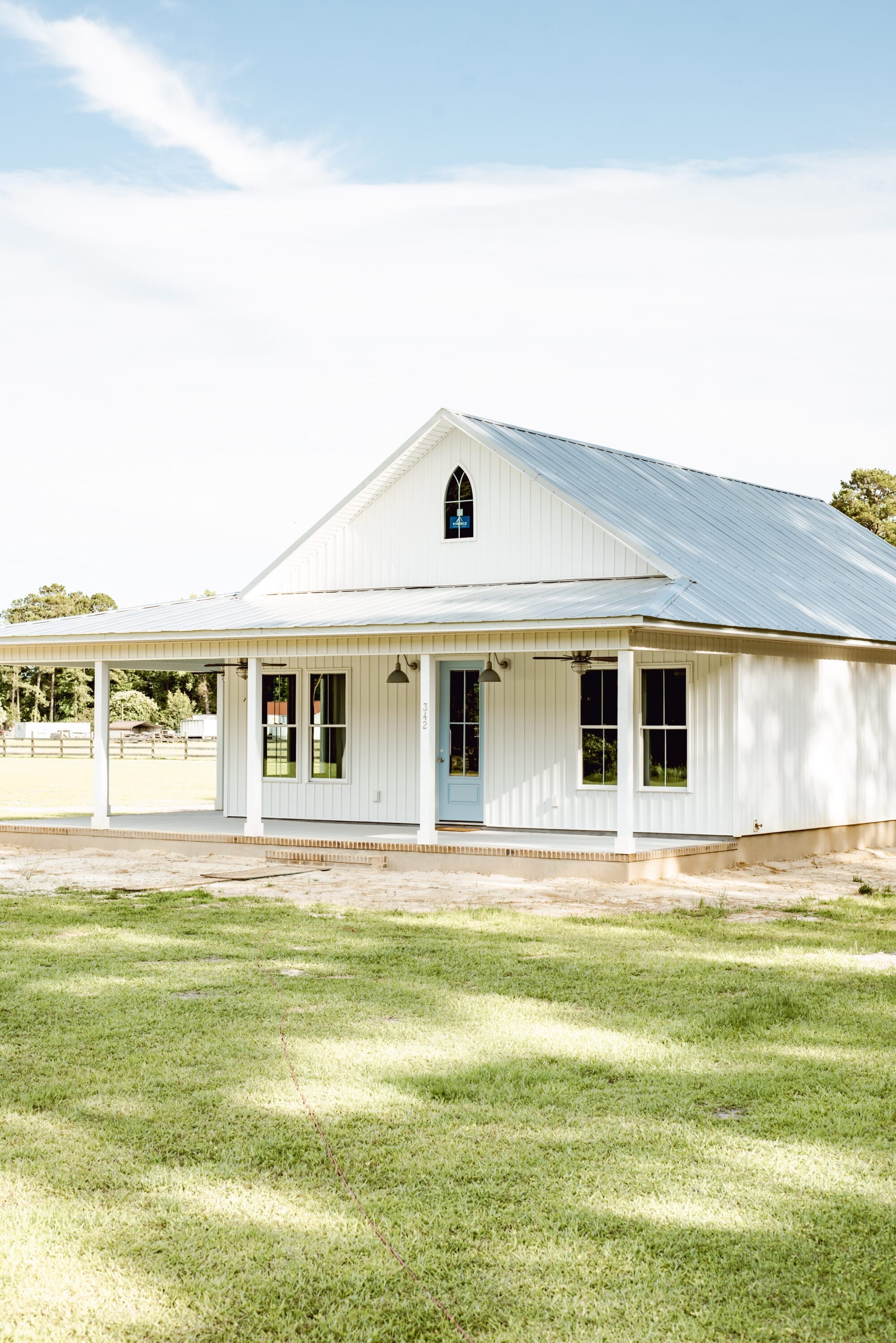 new cottage built to look old with white board and batten siding, metal roof, blue door and a Carpenter Gothic pointed window