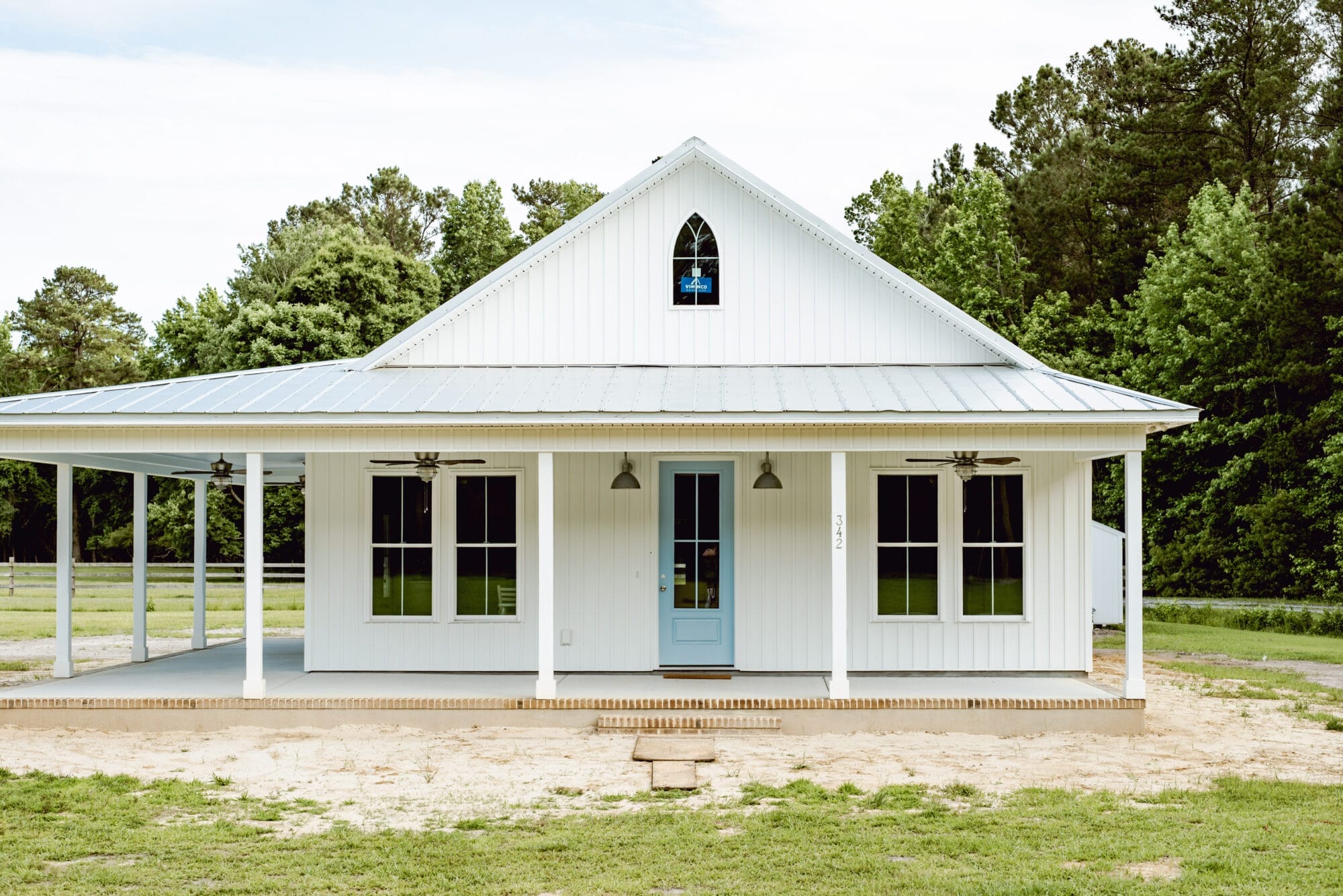 white cottage in the country with a big front porch and blue front door