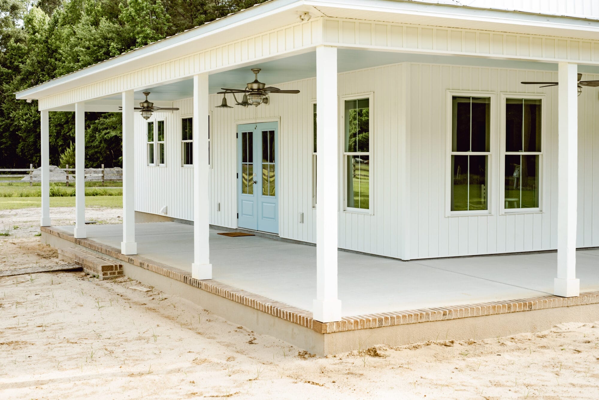 long wraparound porch on a white cottage with blue doors and haint blue porch ceilings