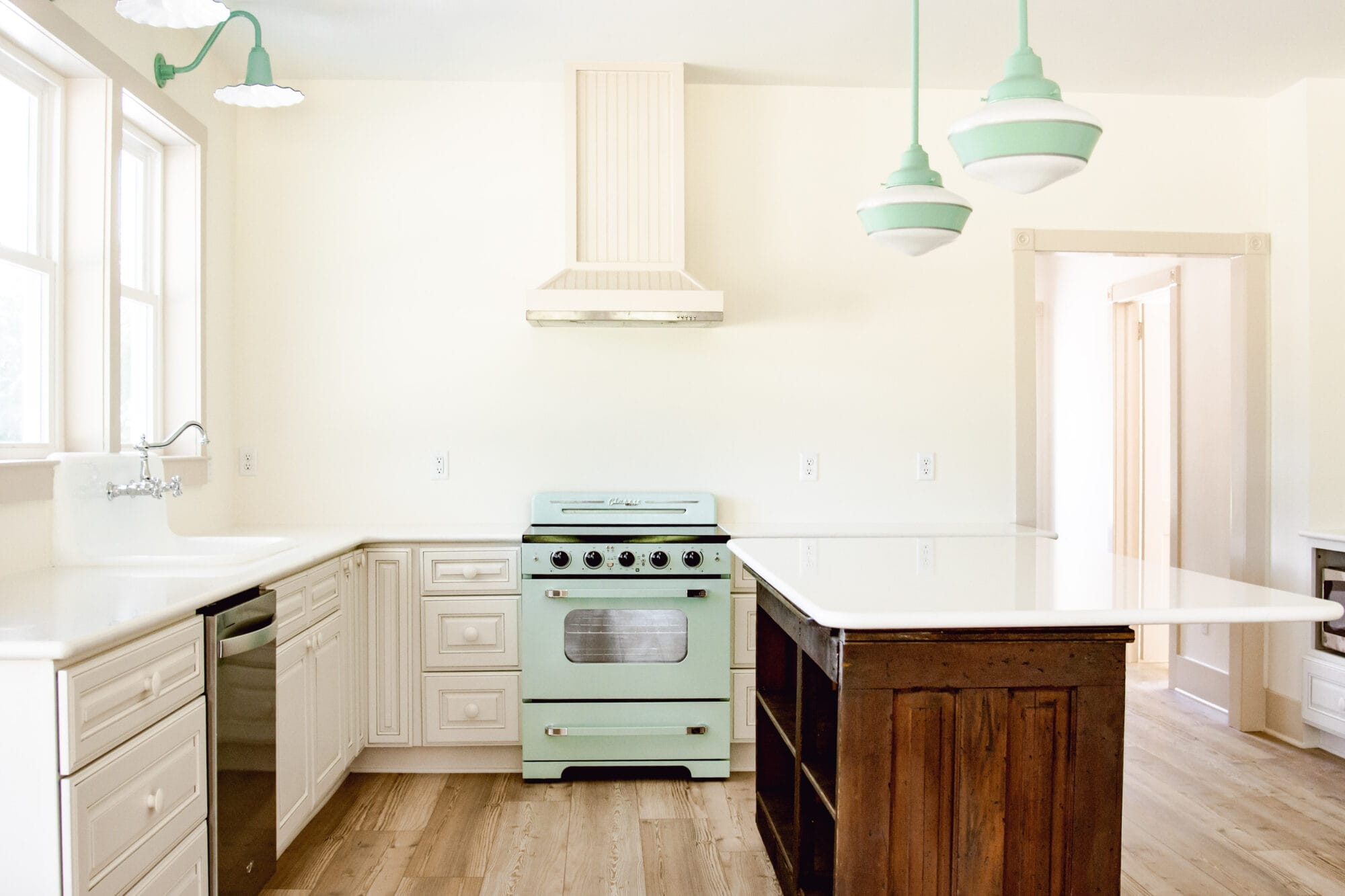 white cottage kitchen with retro mint green stove and schoolhouse lights over the island